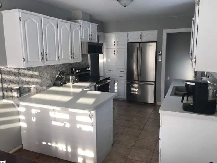 A bright kitchen with white cabinets, light-colored countertops, tiled floors, and stainless steel appliances.