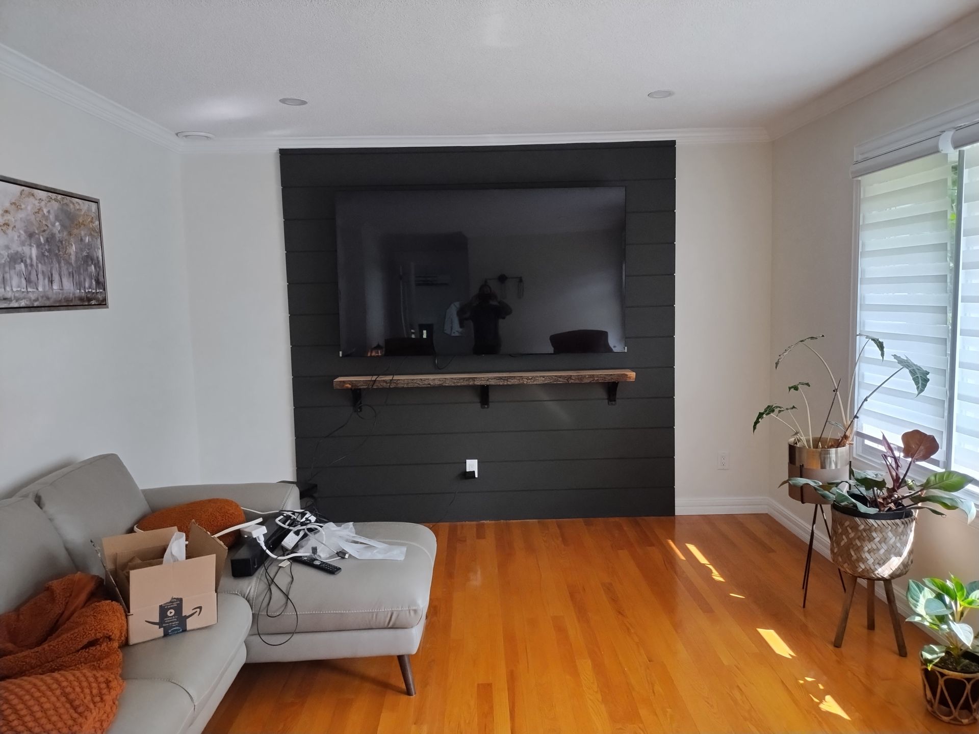 A living room with a grey sofa, a television mounted on a black shiplap accent wall, and a wooden mantel.
