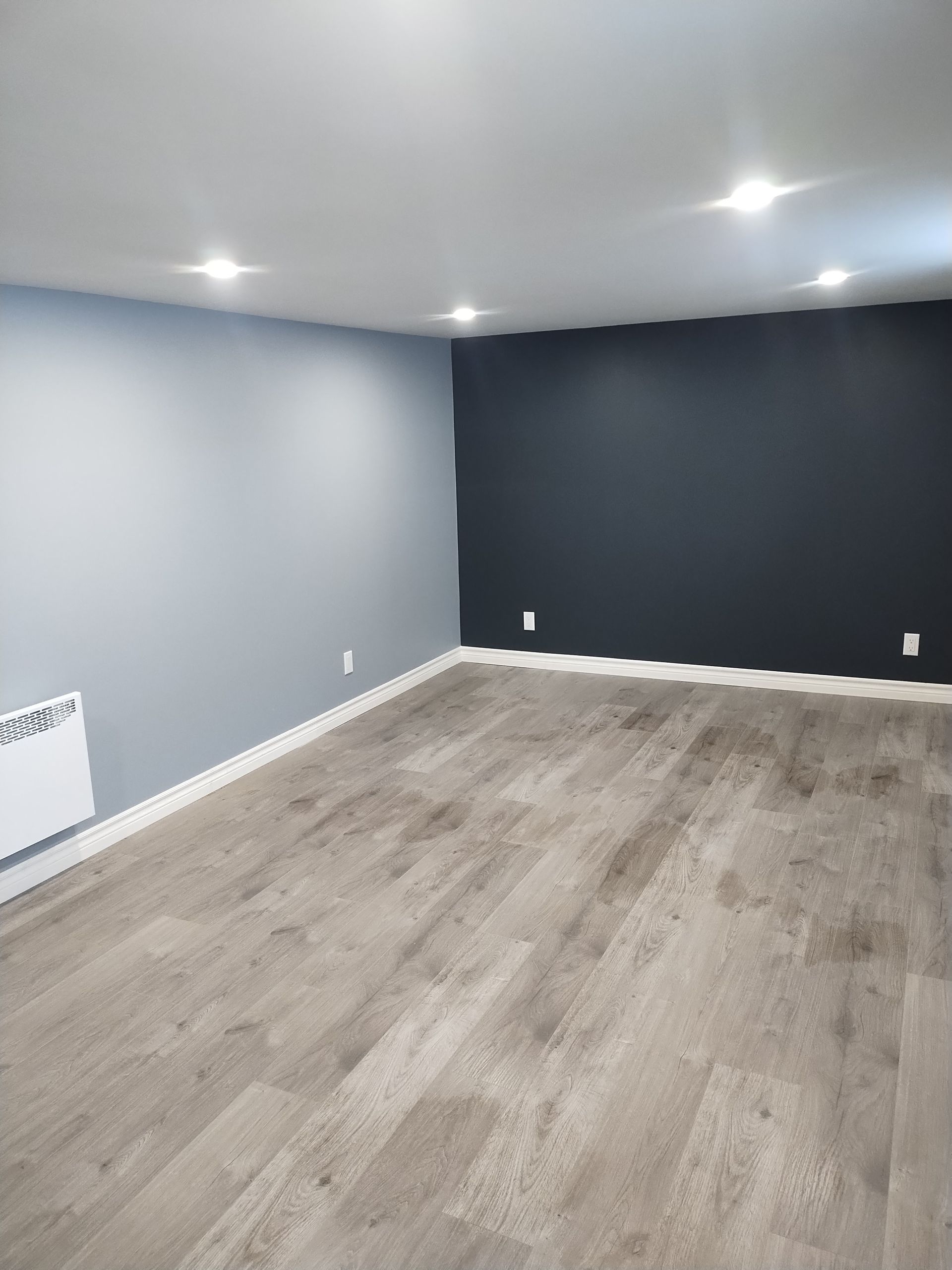 A room featuring light gray flooring, one light blue wall, and one dark navy feature wall with recessed ceiling lights.