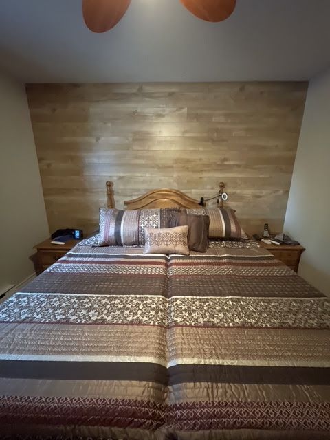A bedroom with a bed featuring a striped brown comforter and a wood-paneled accent wall behind the wooden headboard.