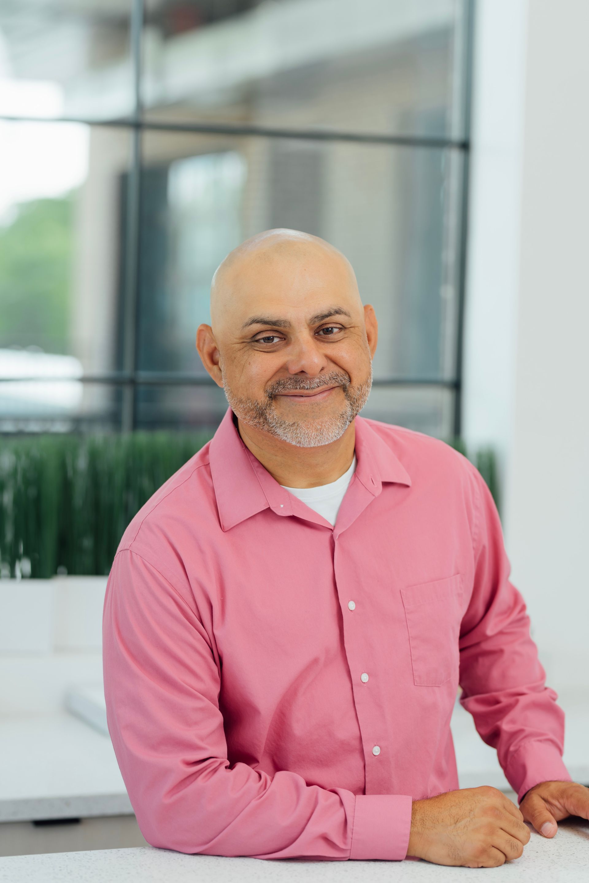 A bald man with a beard is wearing a pink shirt and smiling.