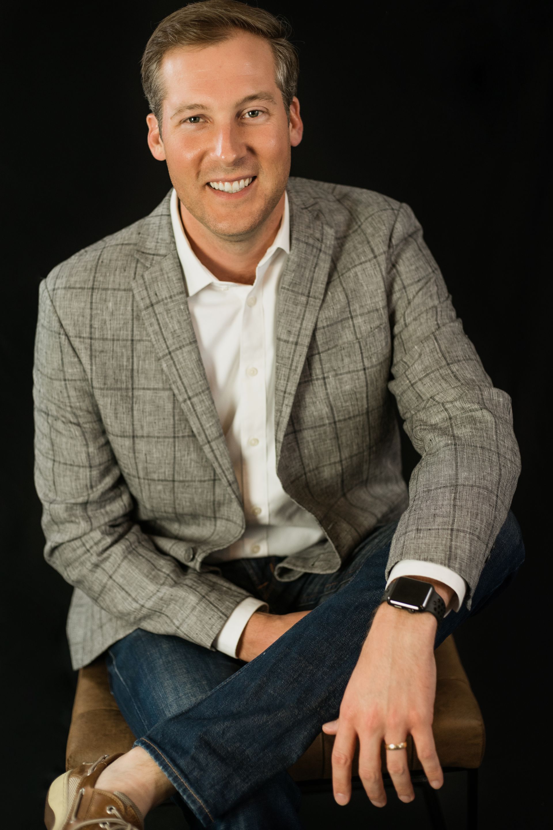 A man in a suit is sitting on a stool with his legs crossed.