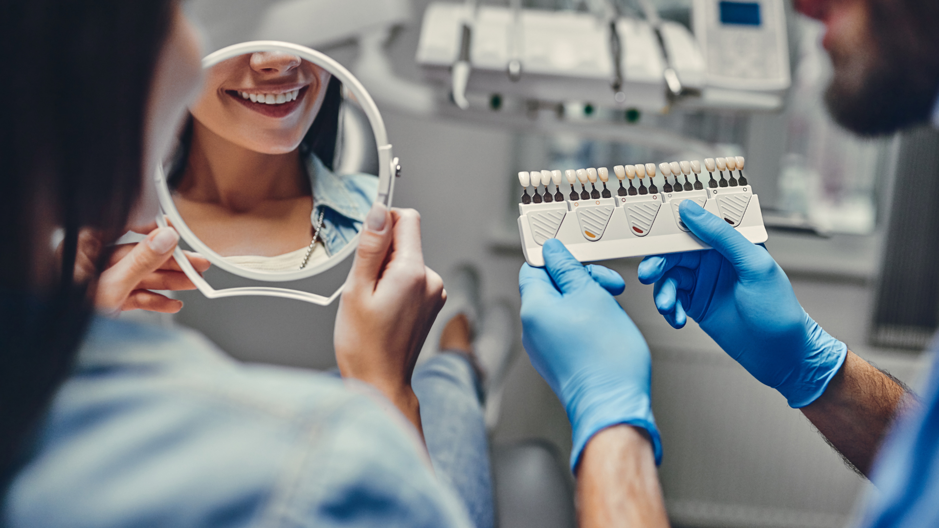 Dentist showing a patient a shade guide to match their teeth while looking in a mirror in a dental office.