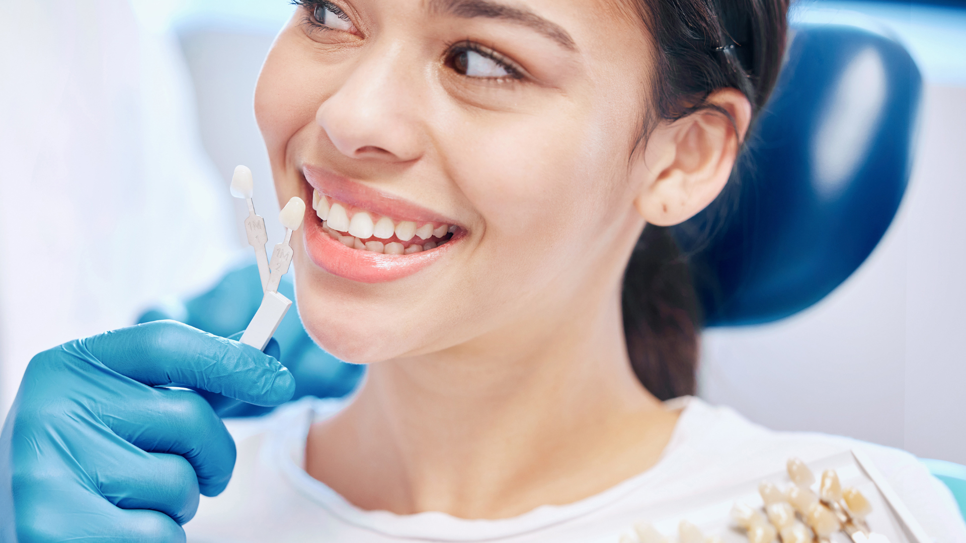 A woman is sitting in a dental chair holding a tooth in her hand.