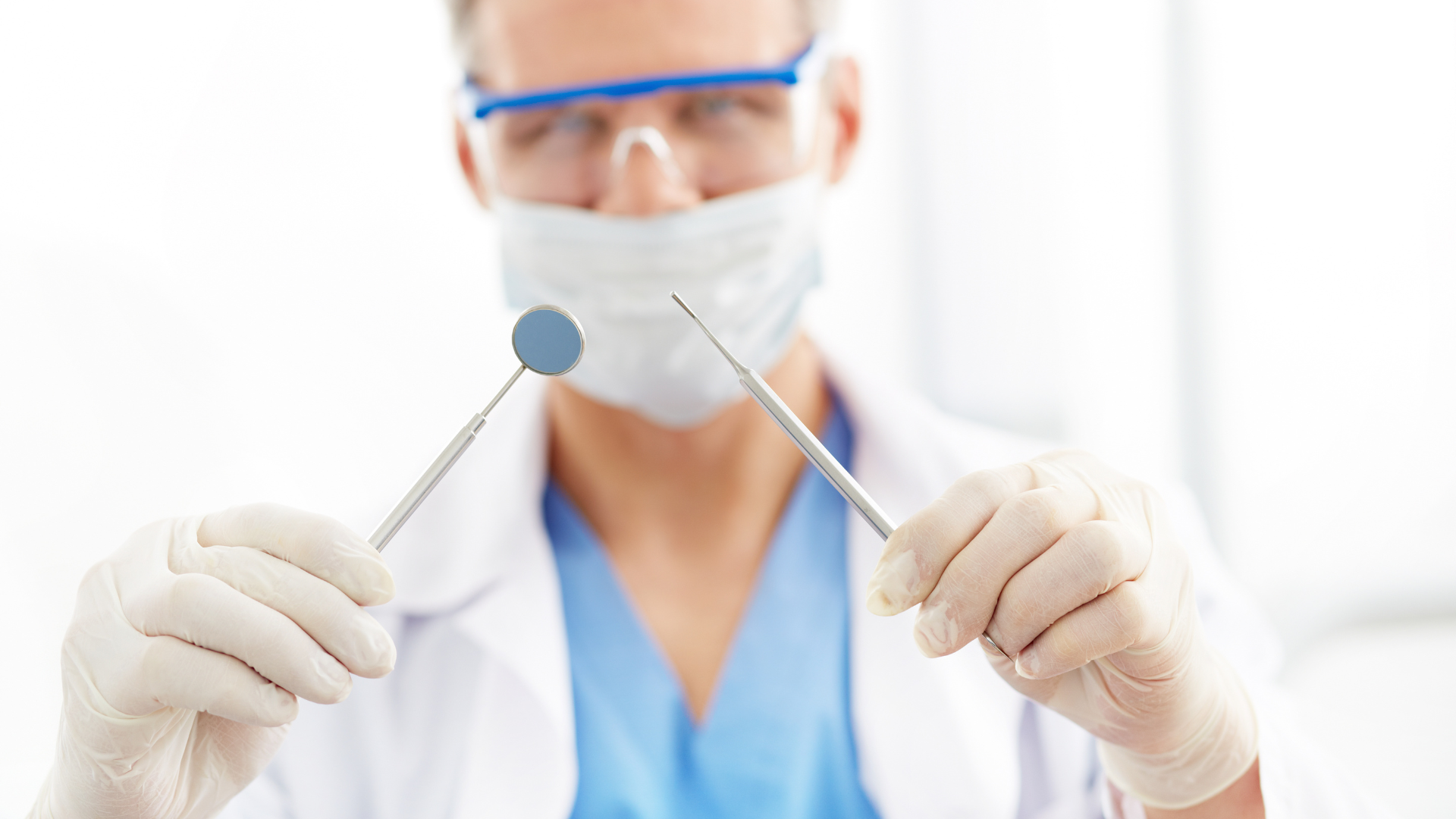 a dentist wearing a mask and goggles is holding a dental mirror and a dental probe .