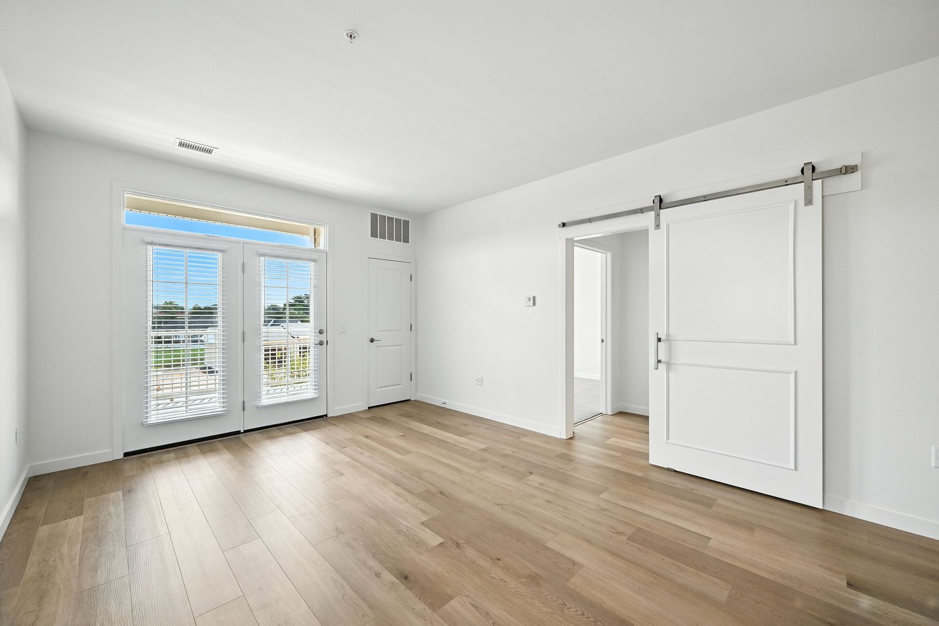 Empty room with wooden floors, French doors, and a sliding barn door.
