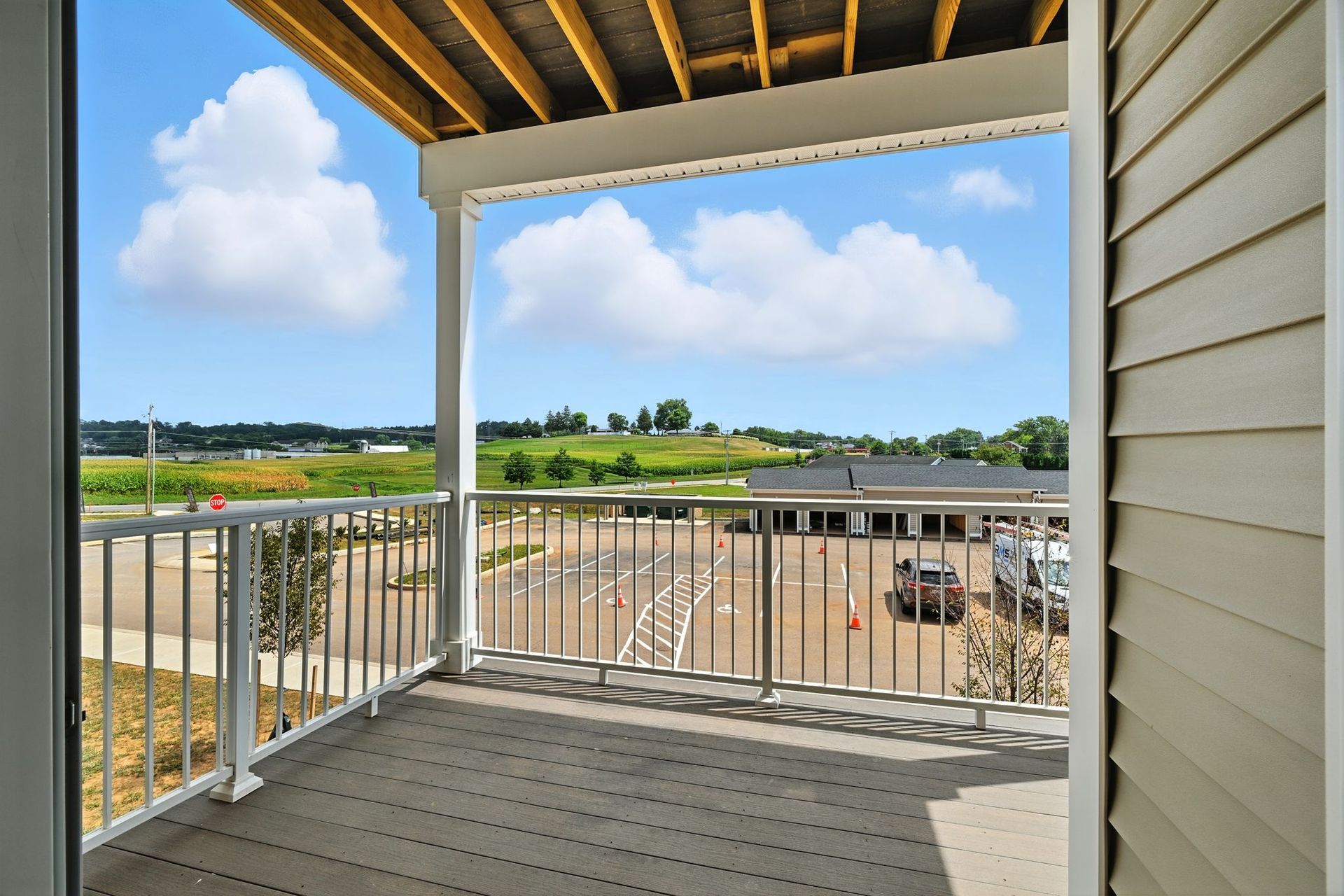 Balcony view: railing and deck, blue sky with clouds, buildings and landscape in the distance.
