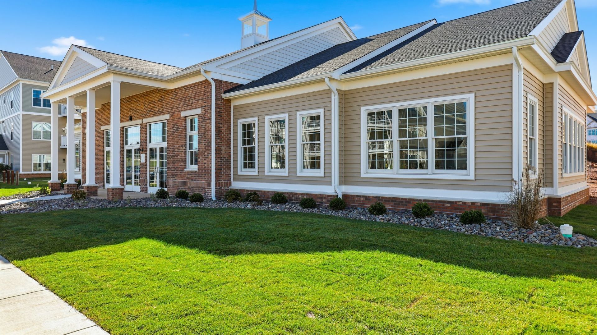 Building with brick and tan siding, white columns, and lush green lawn.