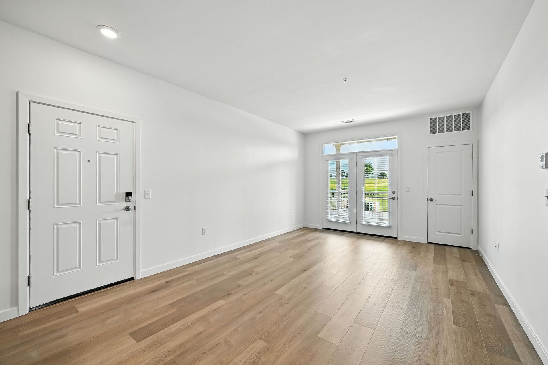 Empty room with light wood floors, white walls, and French doors leading outside.