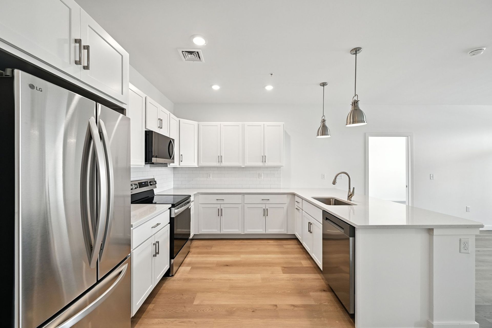 Modern white kitchen with stainless steel appliances, light wood floors, and island.
