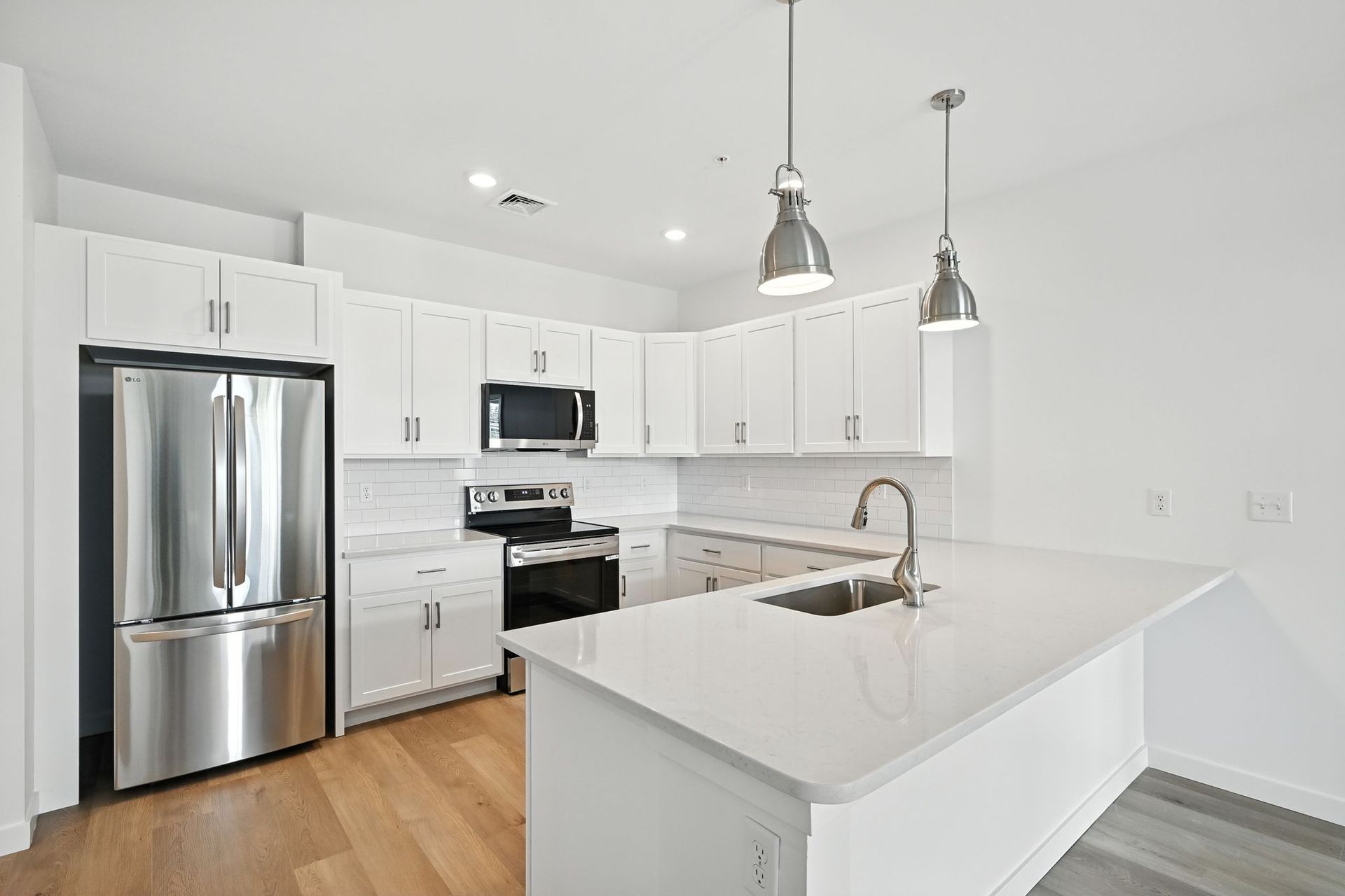 Modern, white kitchen with stainless steel appliances, light wood floors, and quartz countertops.