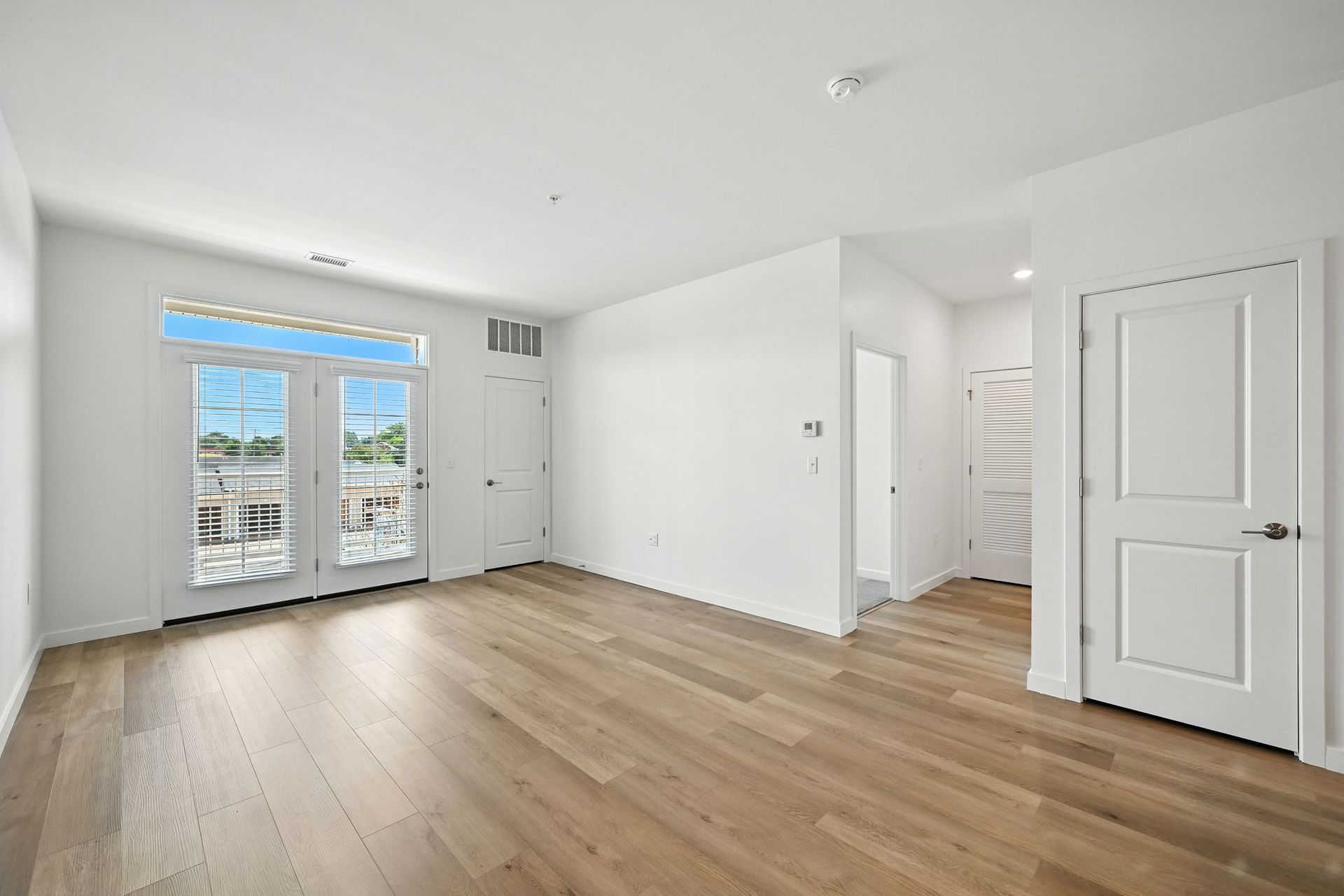 Empty room with hardwood floors, white walls, and French doors to a balcony.