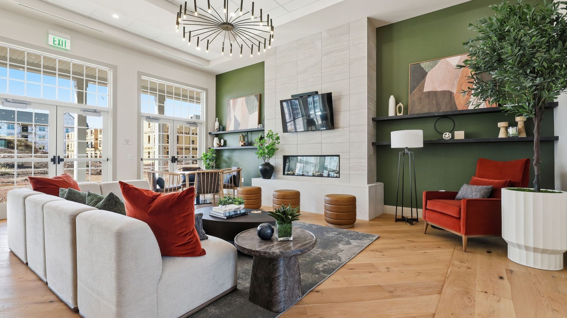 Cozy living room with white sofa, red armchair, green accent wall, fireplace, and large windows.