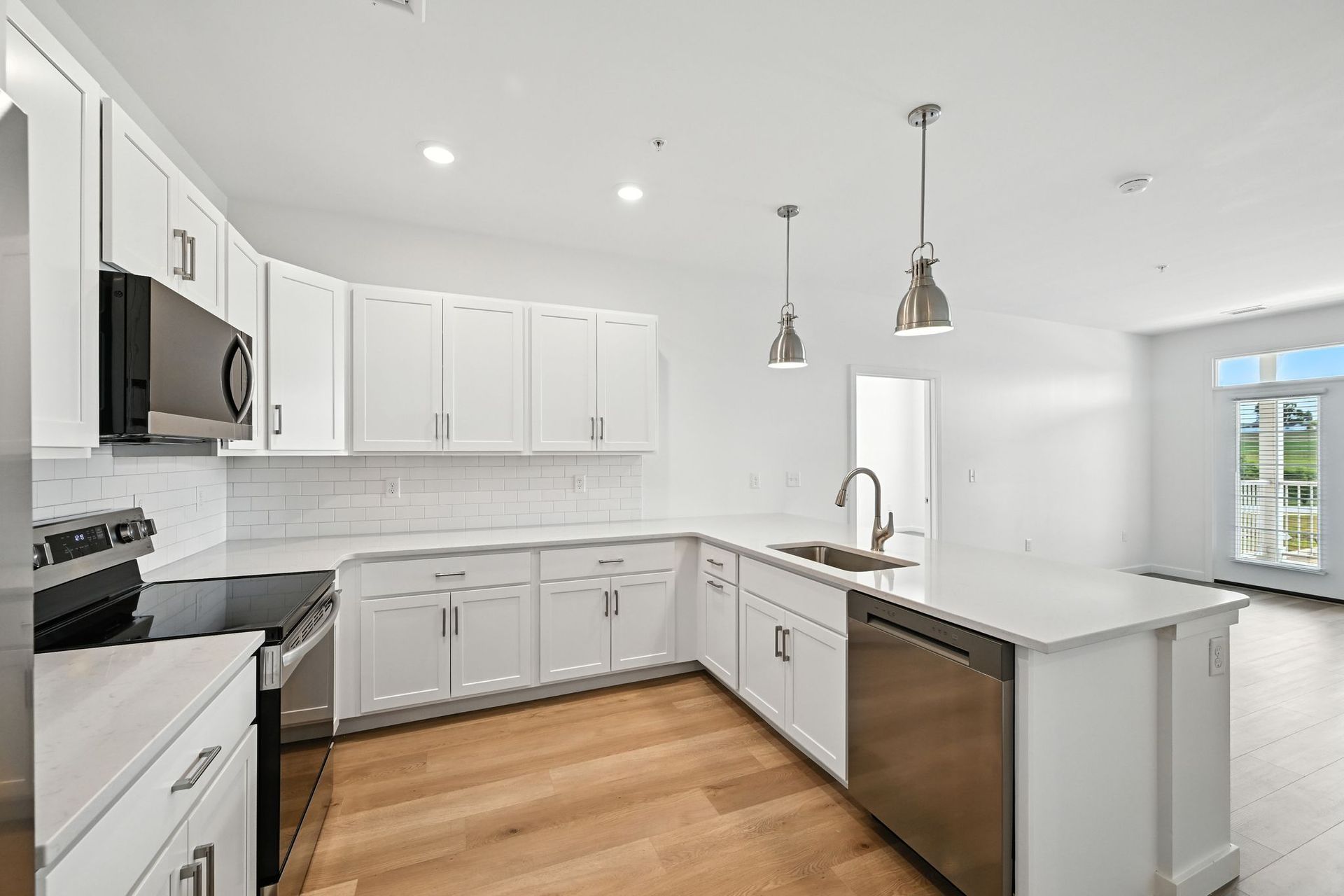 Modern white kitchen with stainless steel appliances, white cabinets, and island with sink.