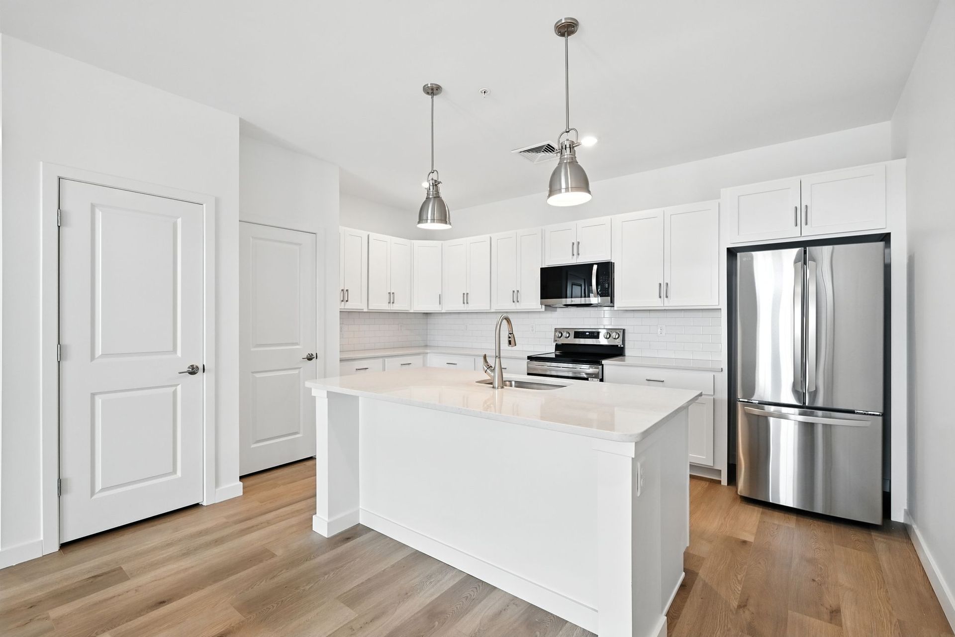 White kitchen with island, stainless steel appliances, and wood flooring.