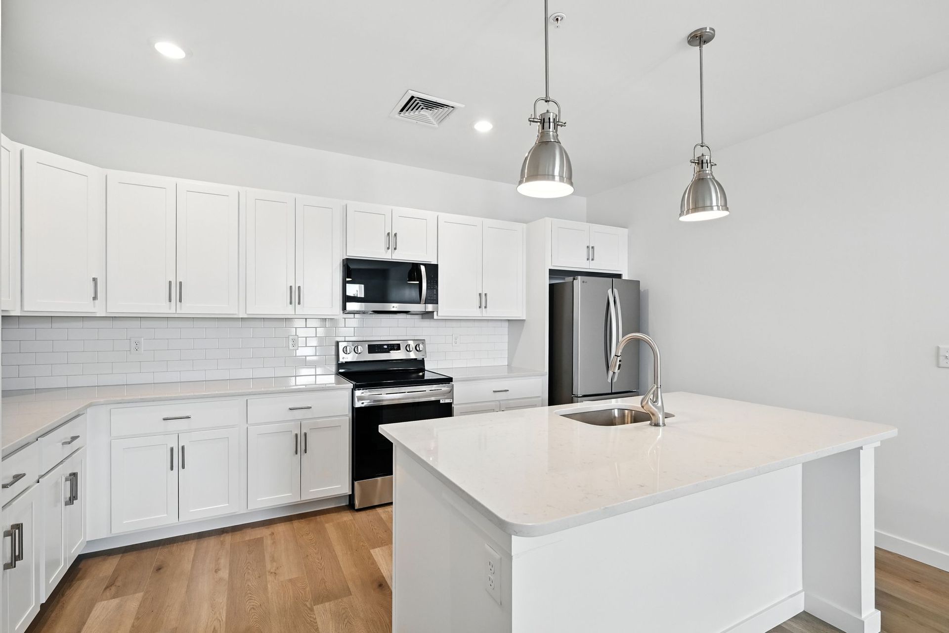 White modern kitchen with island, cabinets, stainless steel appliances, and wood flooring.