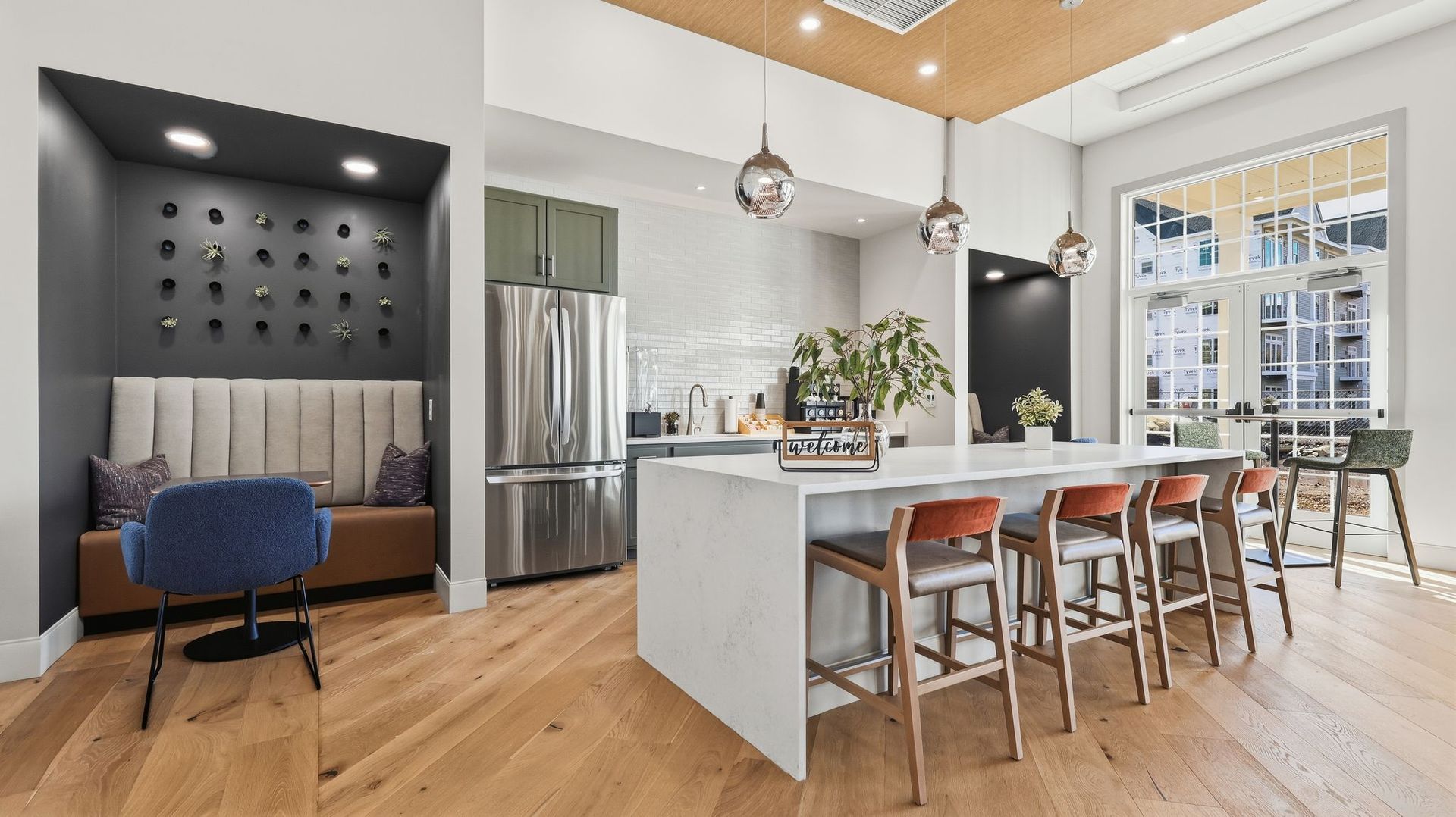 Modern kitchen with island, seating, and built-in booth, stainless steel appliances, and wood flooring.
