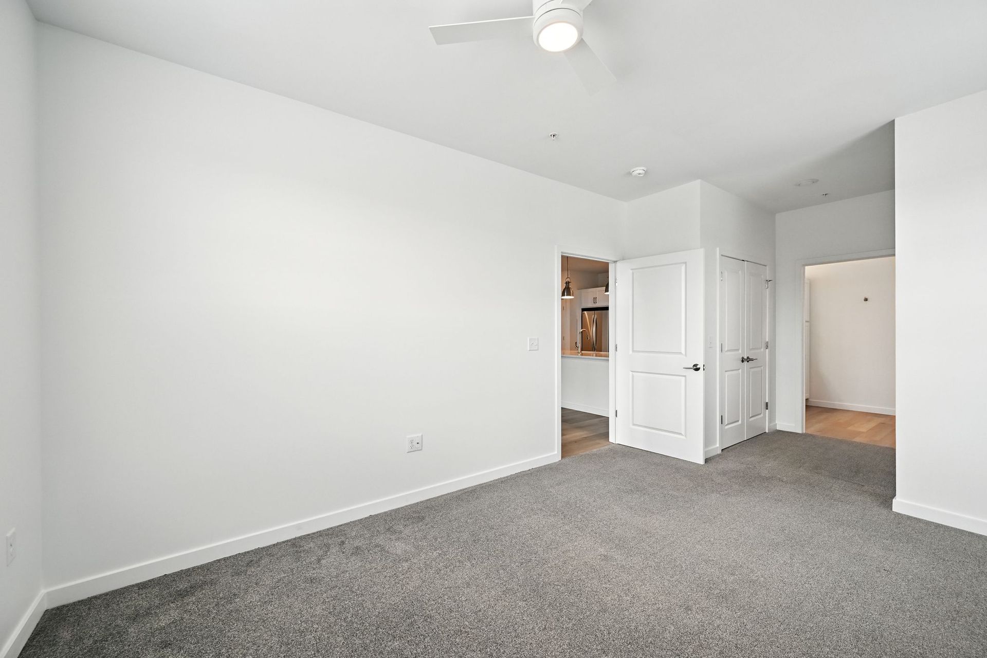 Empty bedroom with gray carpet, white walls, and a door to another room.