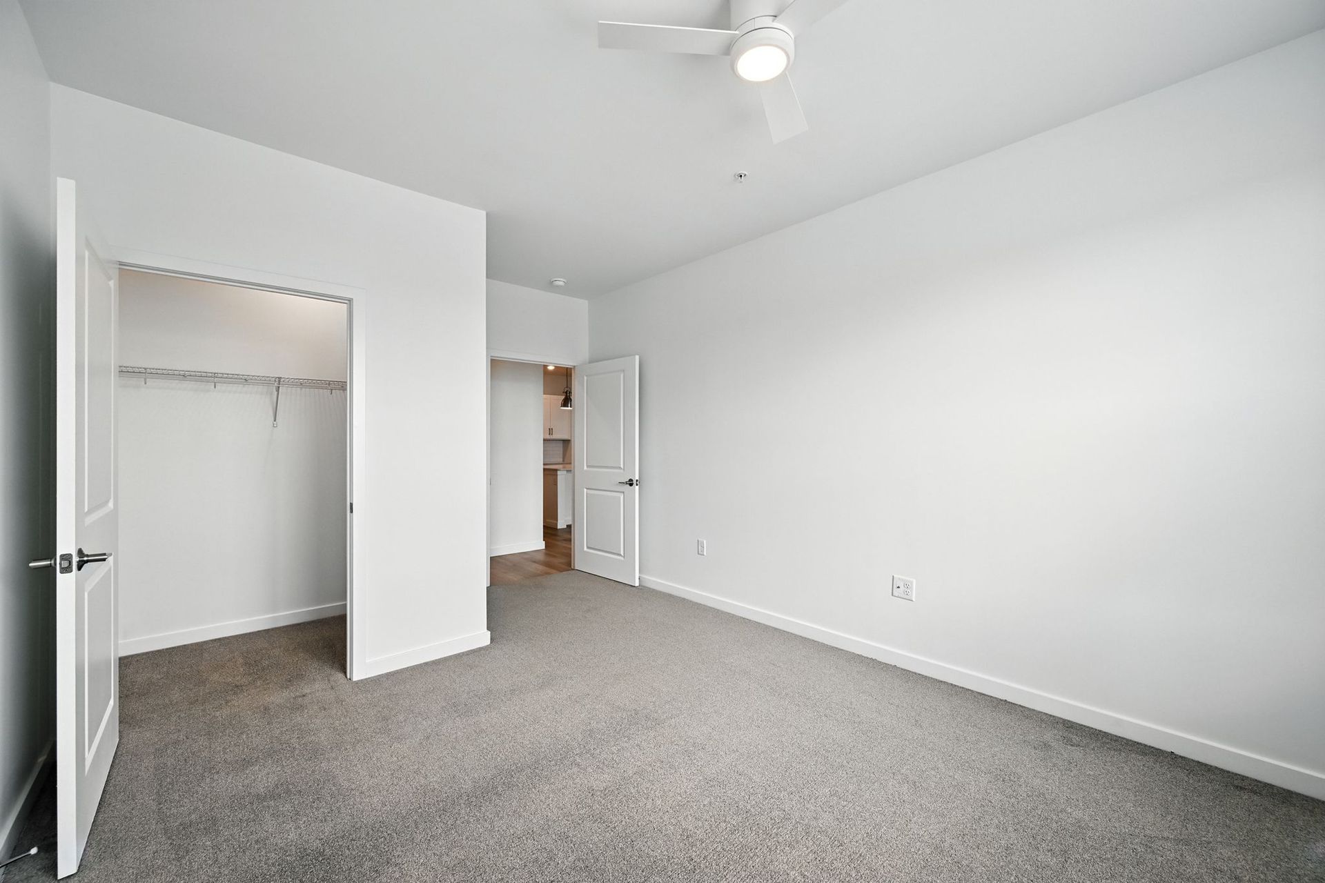 Empty bedroom with carpet, closet, and a doorway to another room. White walls and ceiling.