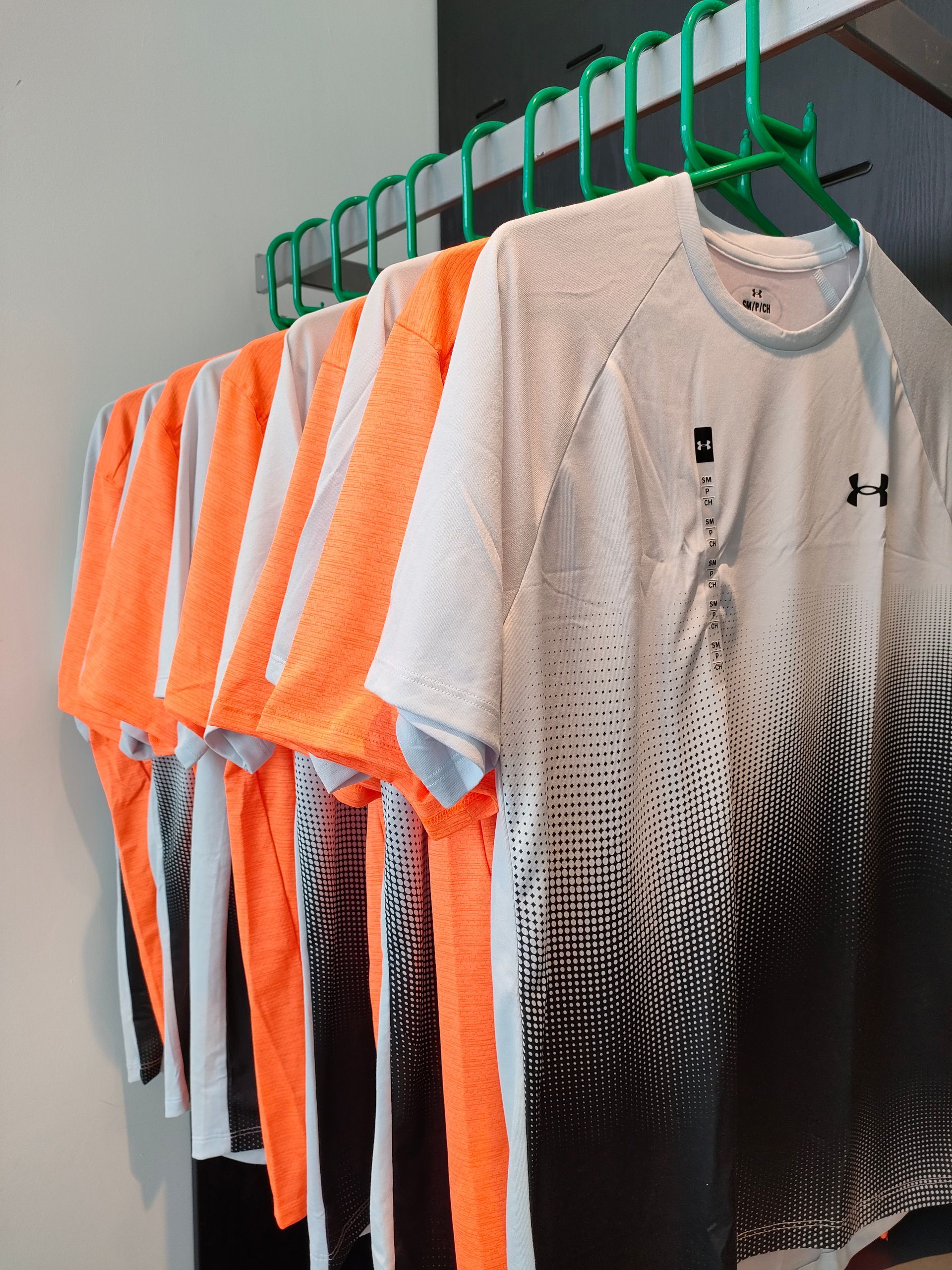 una fila di t-shirt appese a un gancio verde