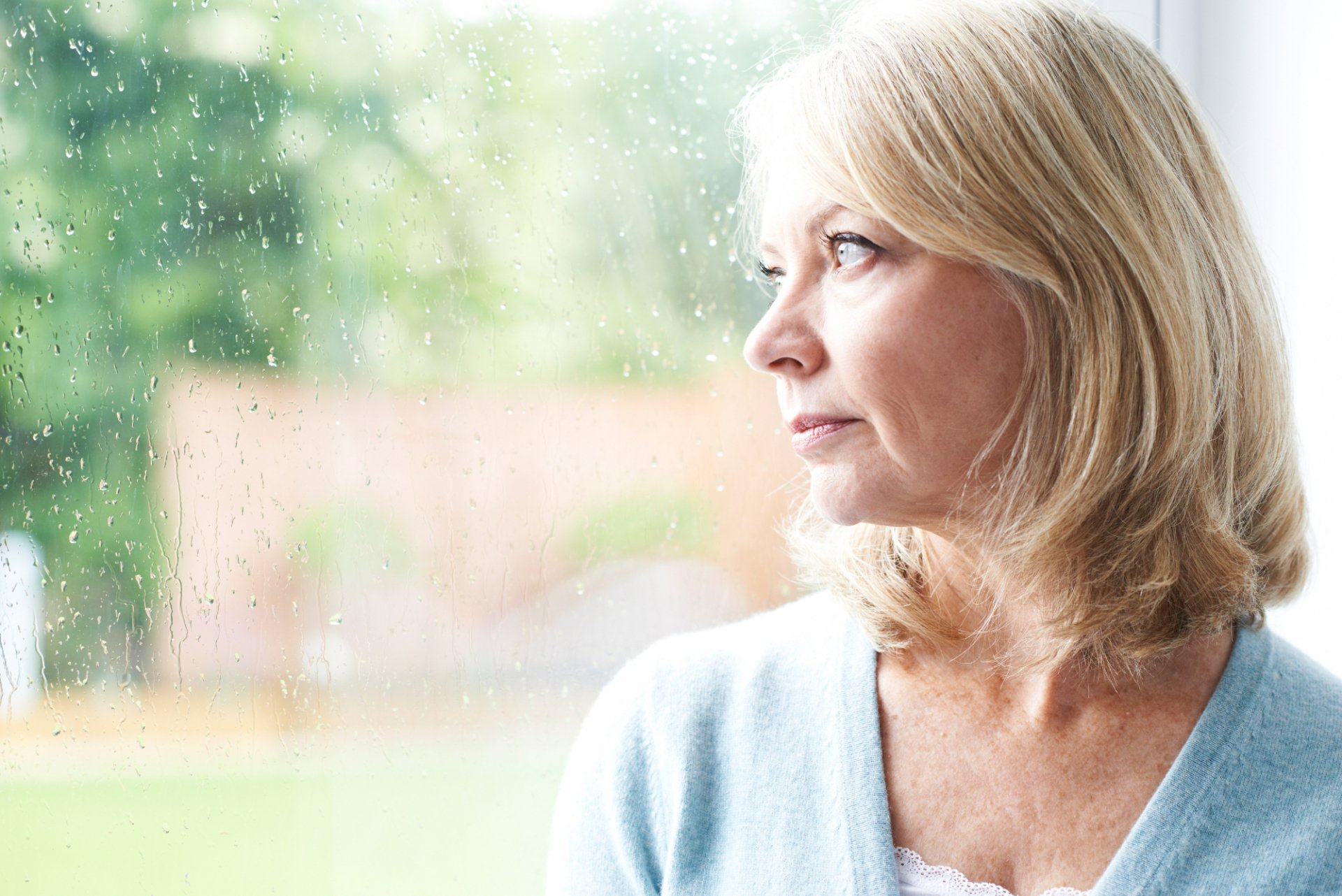 pensive senior woman looking out rainy window
