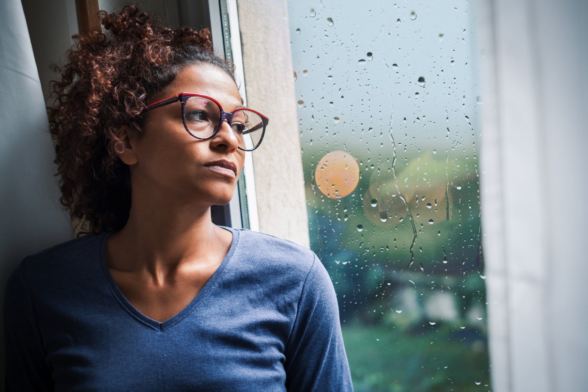 sad woman in 30s looks out window raining