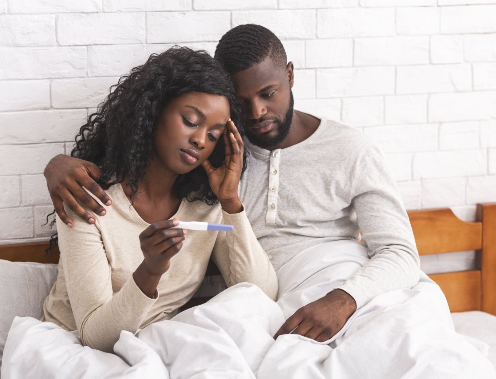 sad couple in bed looking at negative pregnancy test
