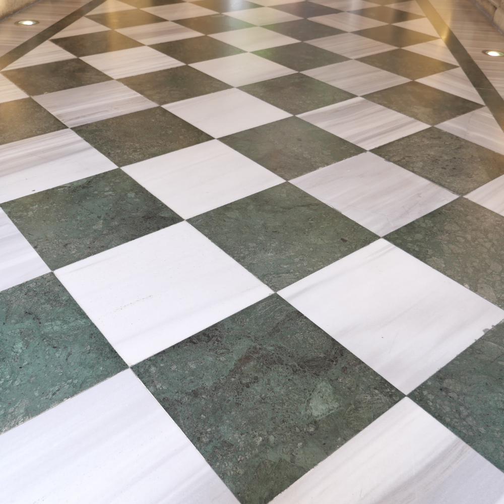 A floor featuring a repeating checkerboard pattern of alternating square white marble and dark green stone tiles.