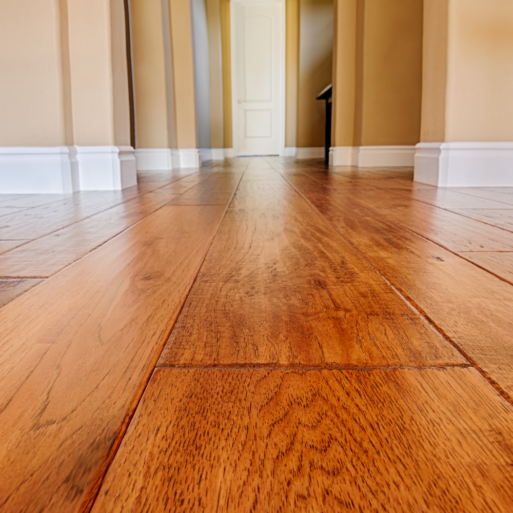 A low-angle view of a wooden hallway floor with warm-toned planks leading toward a white door.