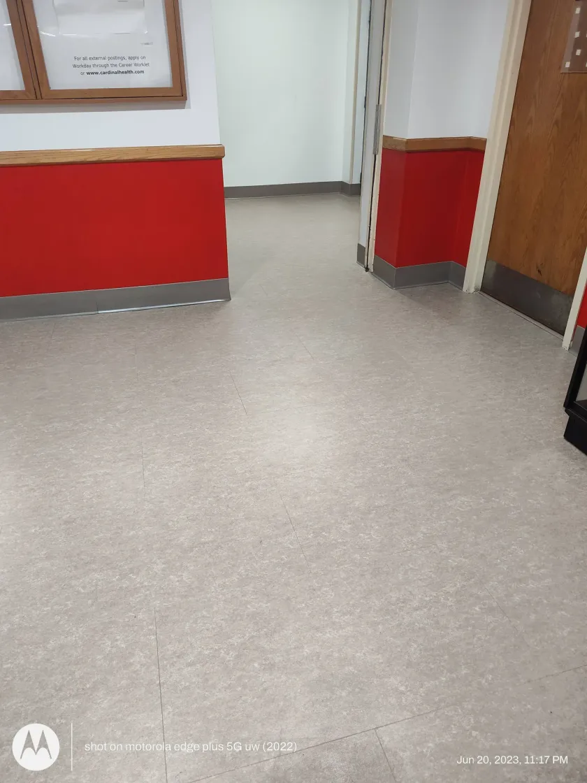 A low-angle view of a wooden hallway floor with warm-toned planks leading toward a white door.