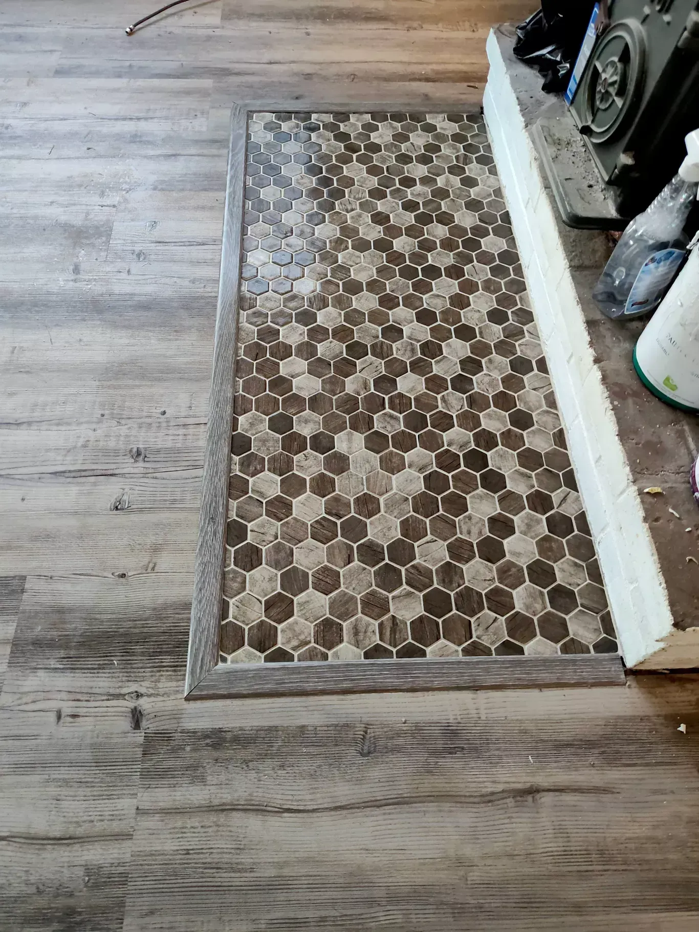 A floor transition showing a mosaic of brown and tan hexagonal tiles bordered by wood-look laminate flooring.