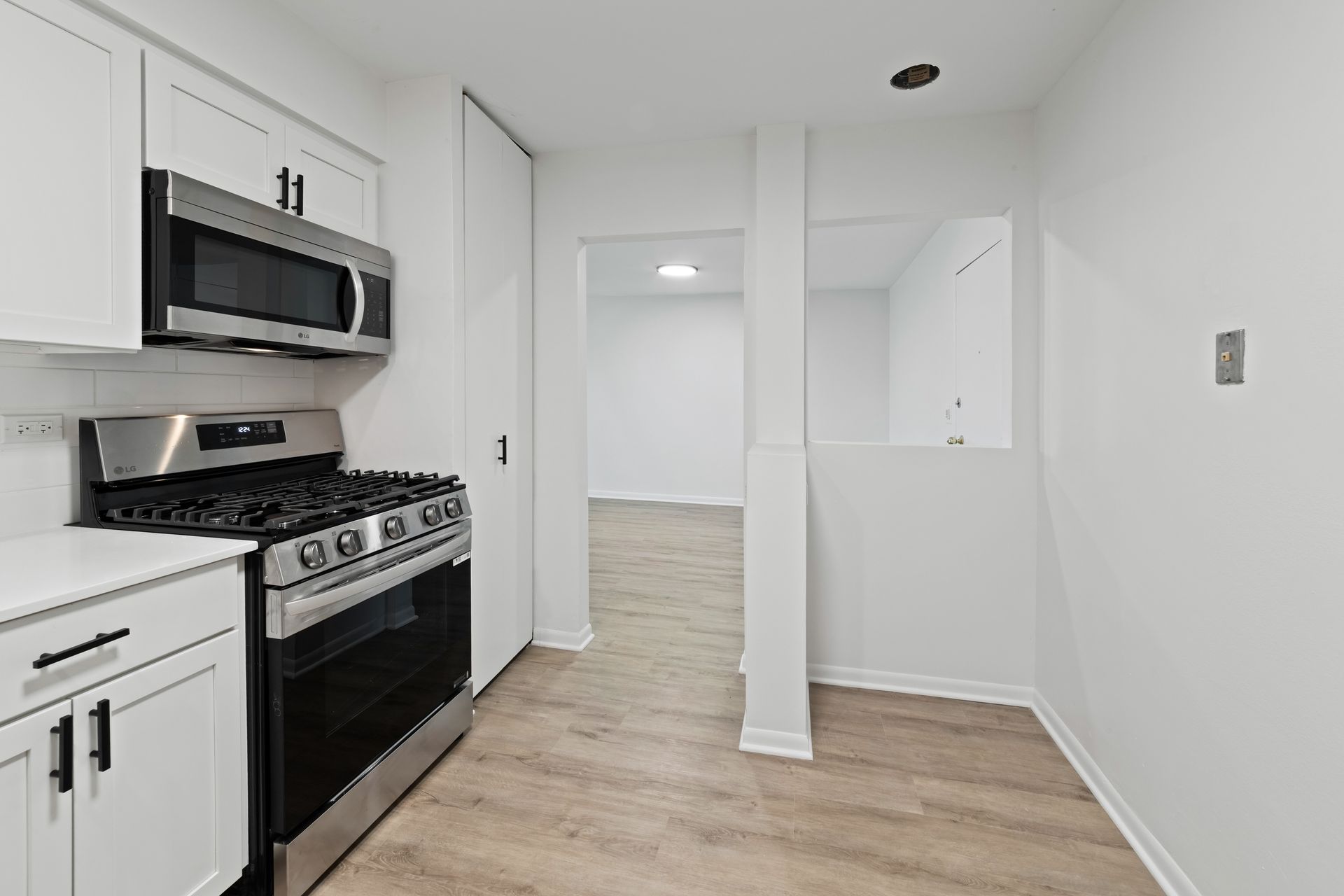 White kitchen with stainless steel appliances and open doorway to another room.