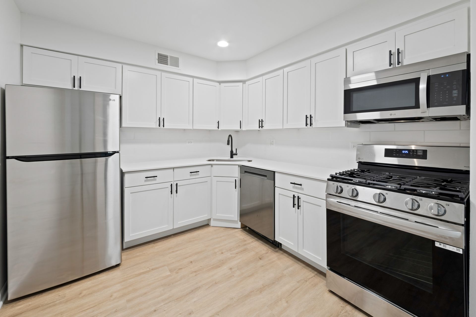 White kitchen with stainless steel appliances, light wood-look floor, and white countertops.