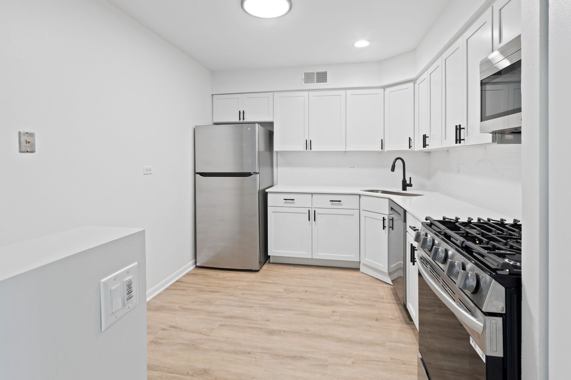 Kitchen with white cabinets, stainless steel appliances, and wood-look flooring.