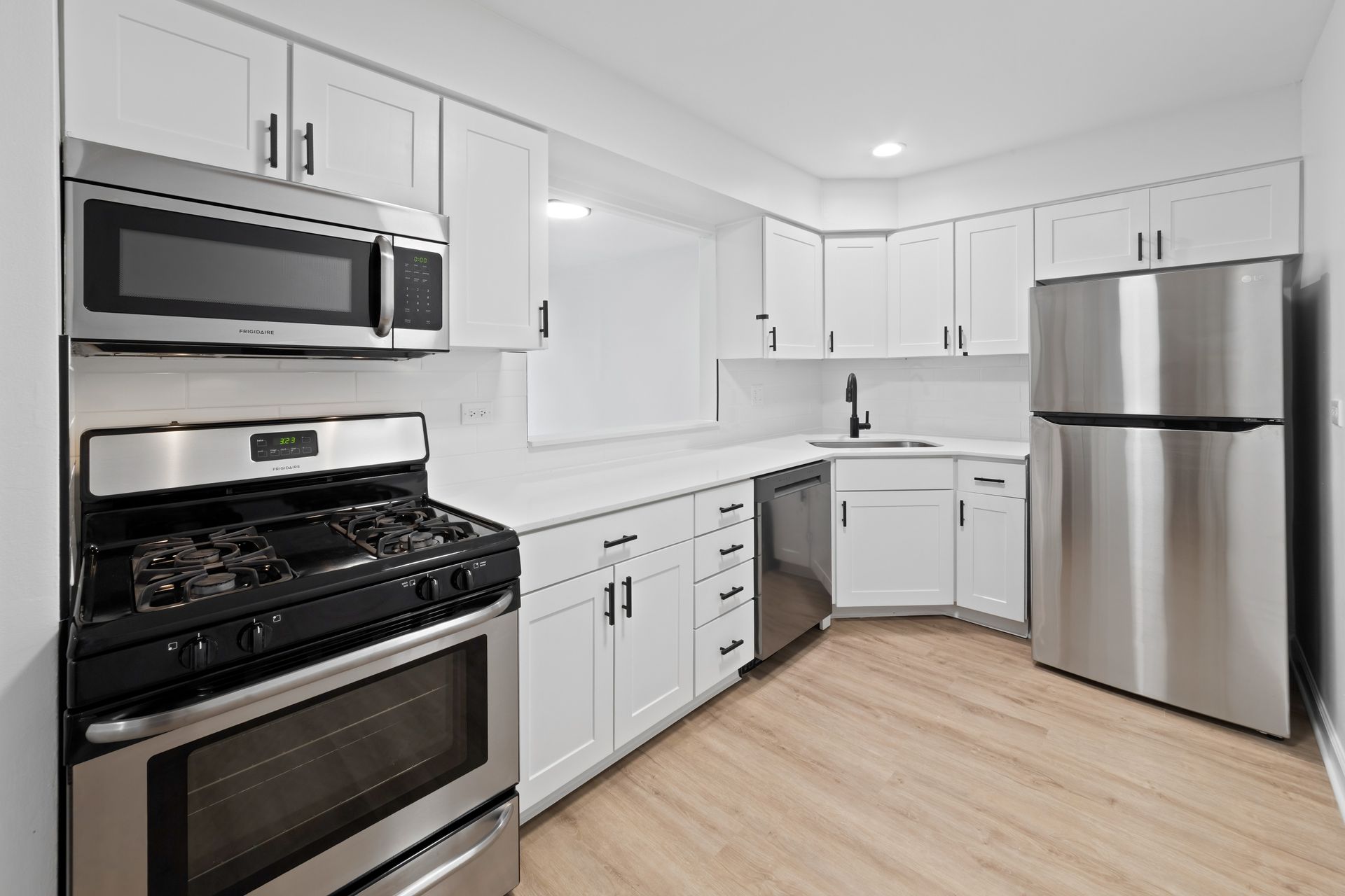 Modern kitchen with white cabinets, stainless steel appliances, and light wood-look flooring.