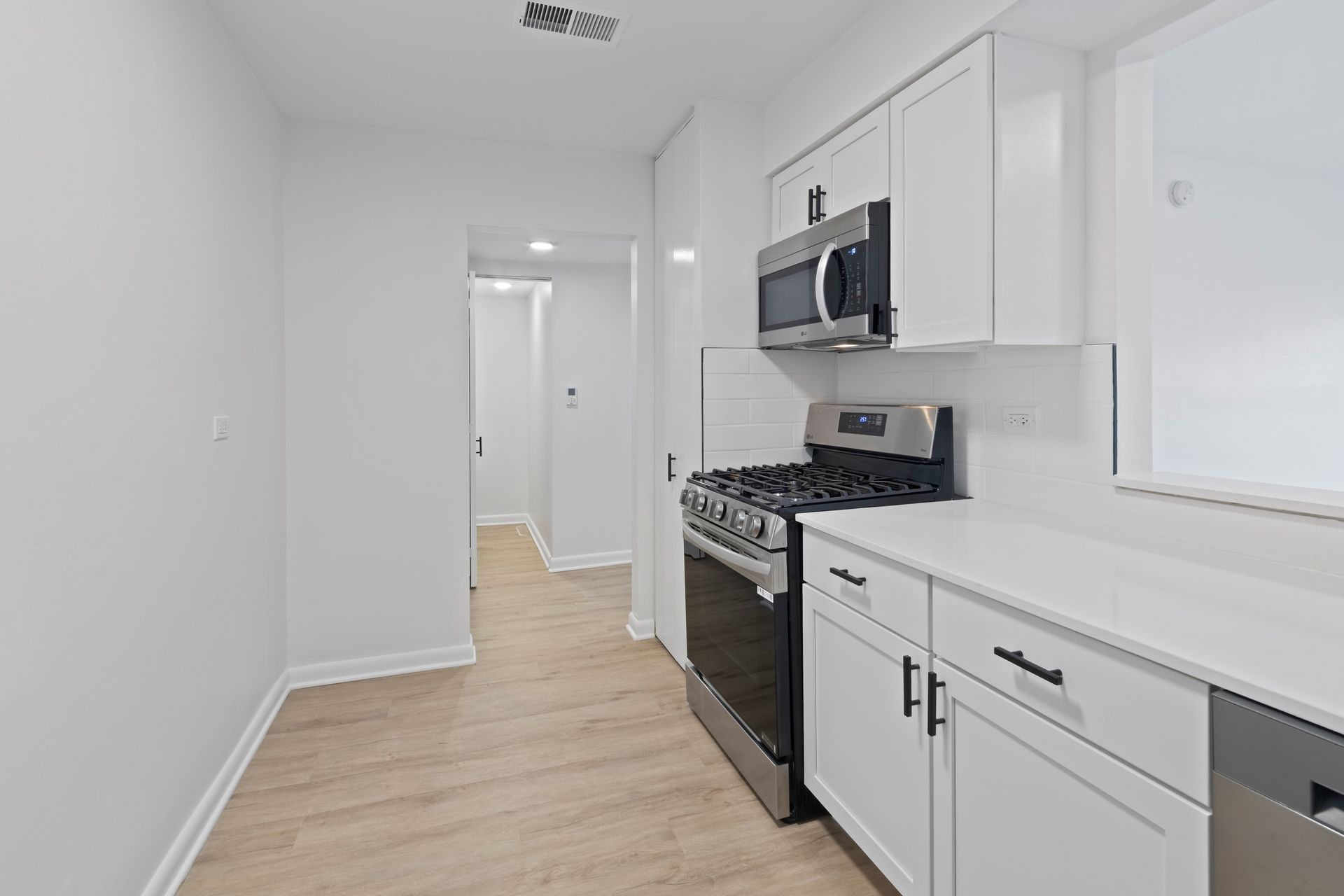 White kitchen with stainless steel appliances, white cabinets, and light wood flooring.