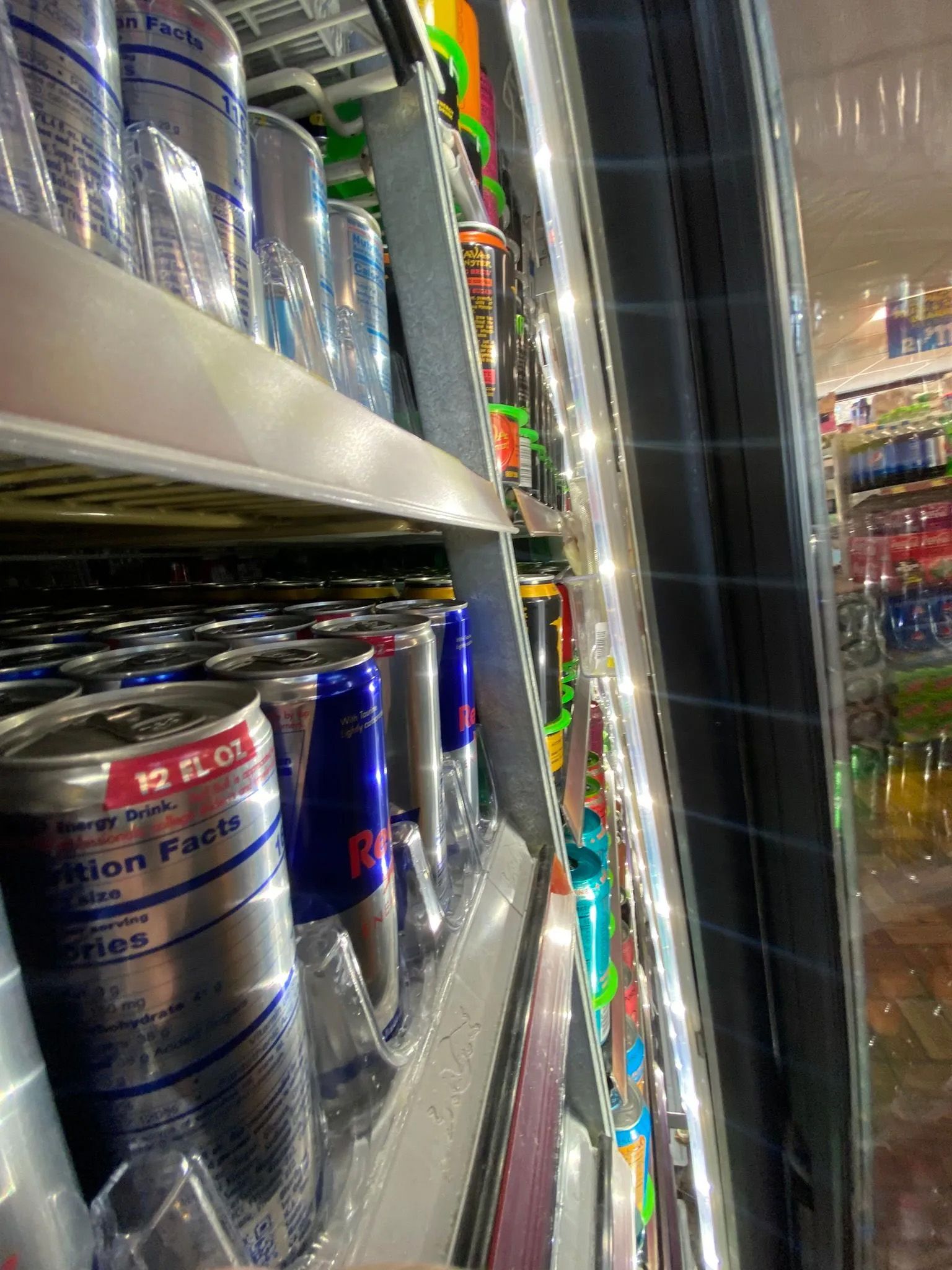 A refrigerator filled with cans of red bull in a store.