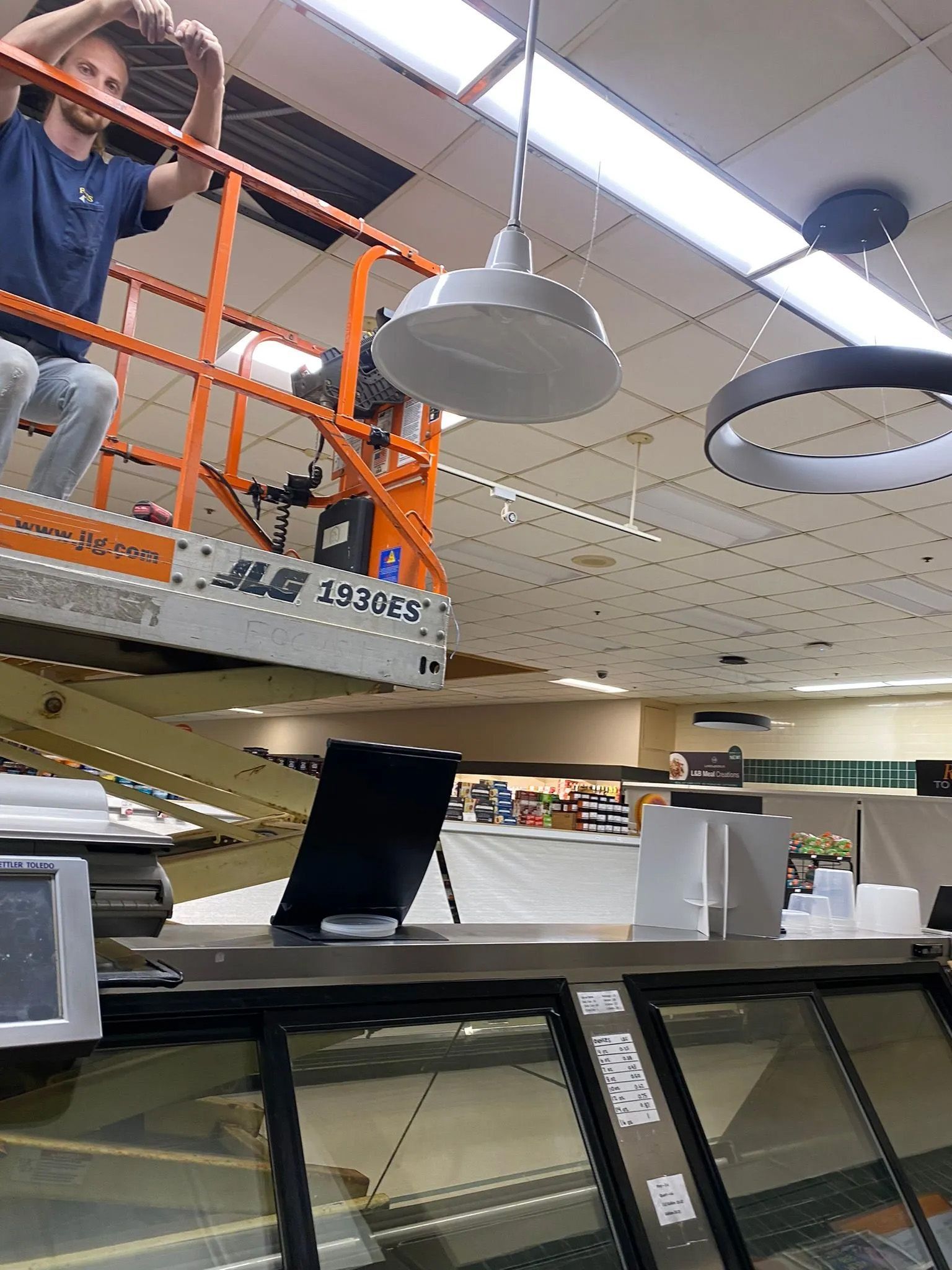 A man is sitting on a lift working on the ceiling of a building.
