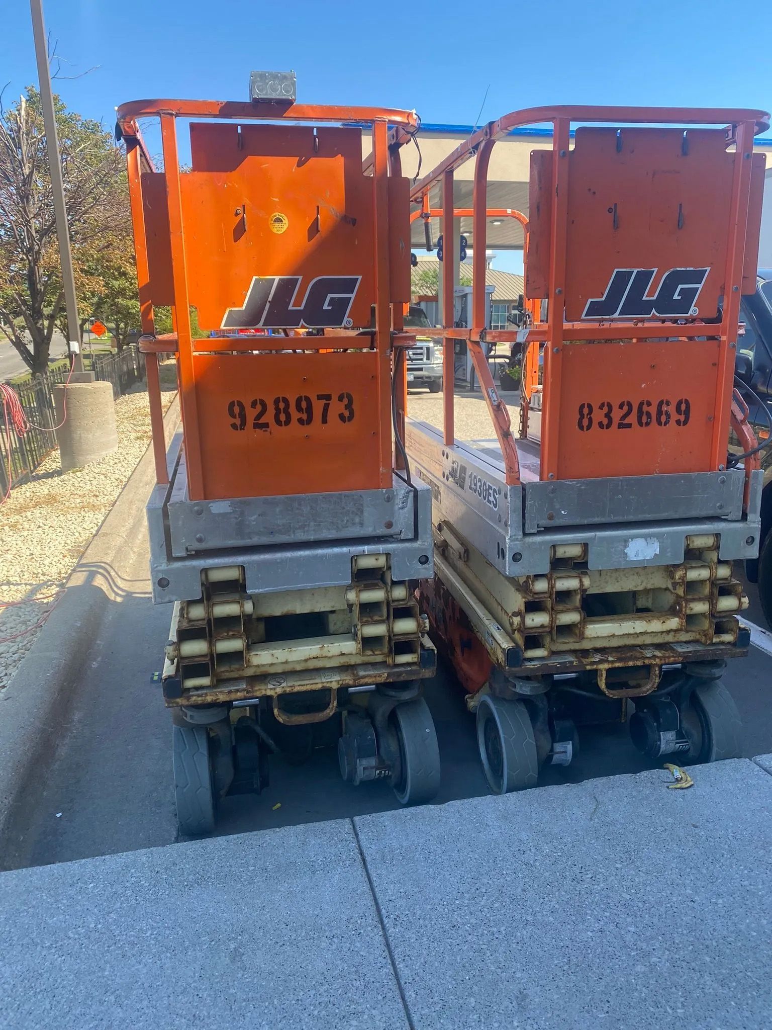 Two orange jlg scissor lifts are parked on the side of the road.