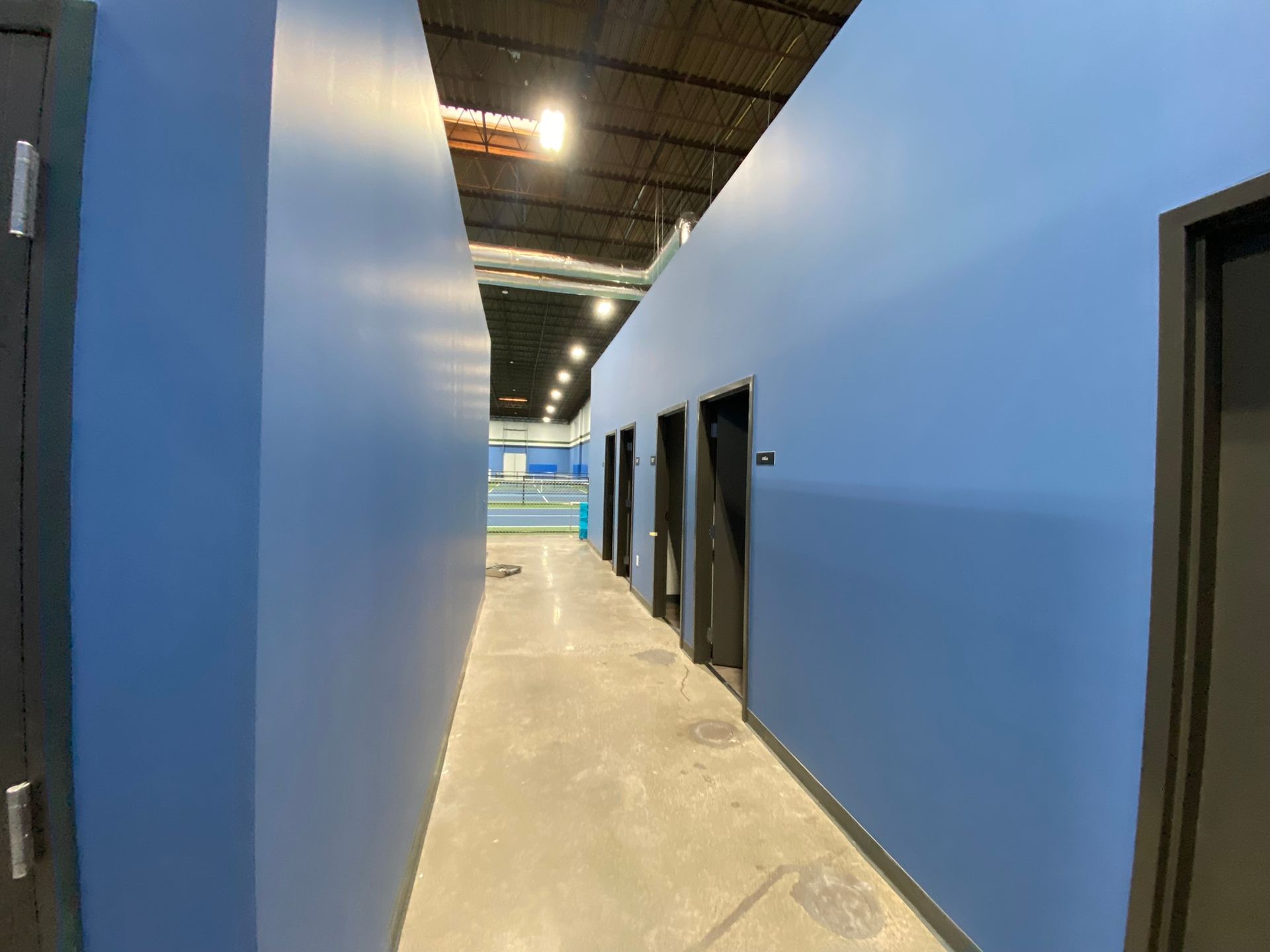 A long hallway with blue walls and black doors in a building.
