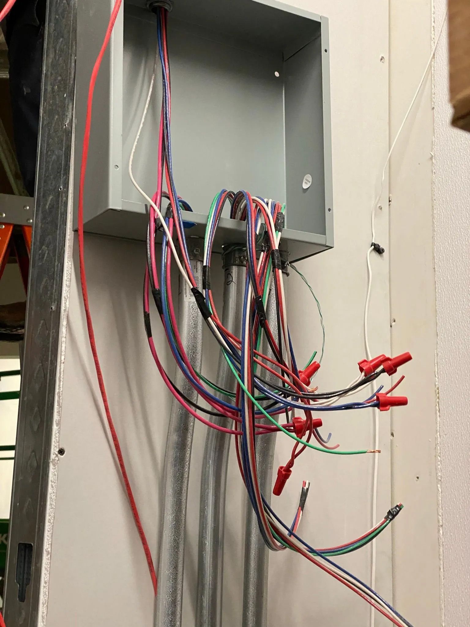 A bunch of wires are hanging from a box on a wall.