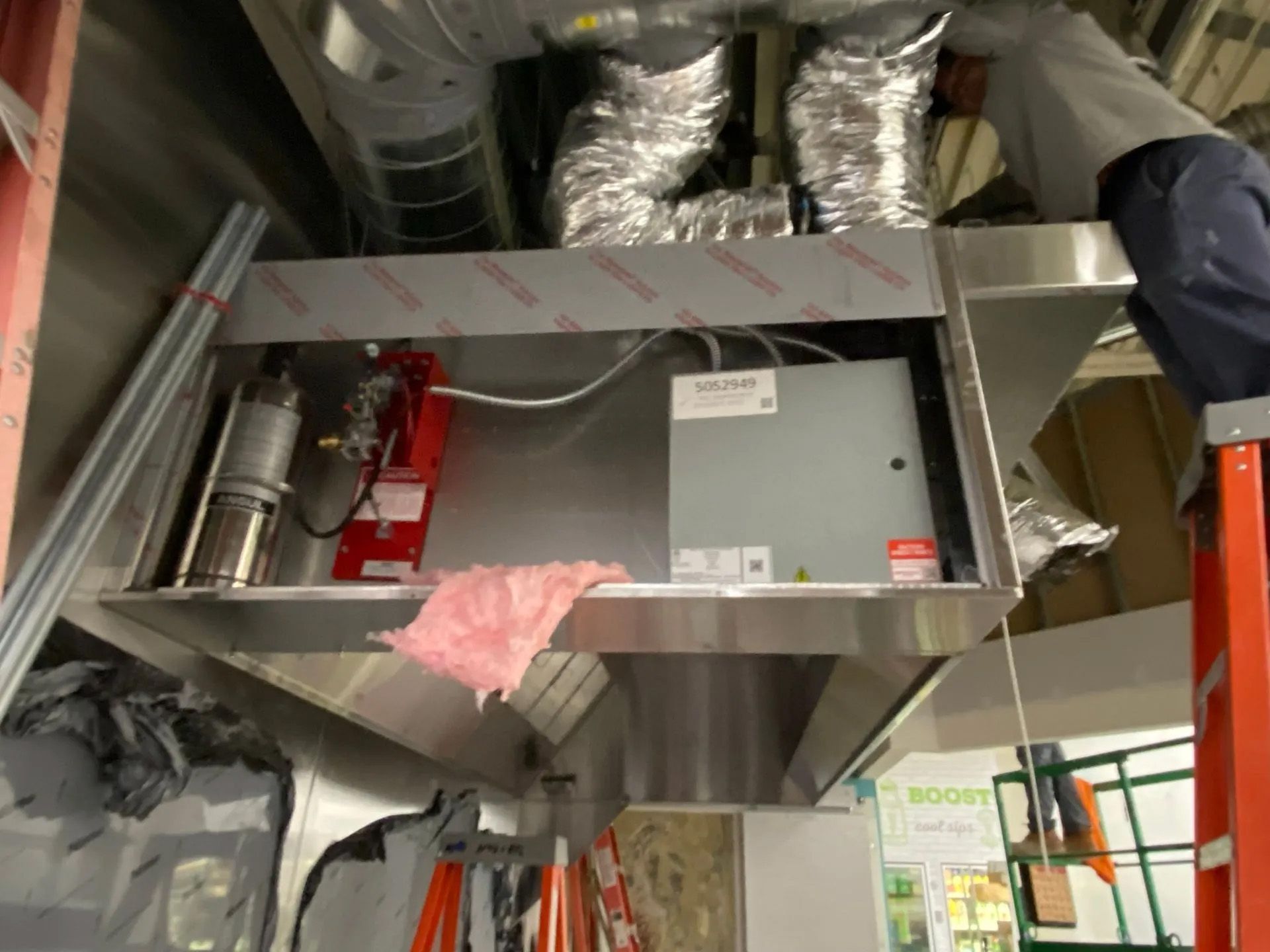 A man is standing on a ladder working on a ventilation system