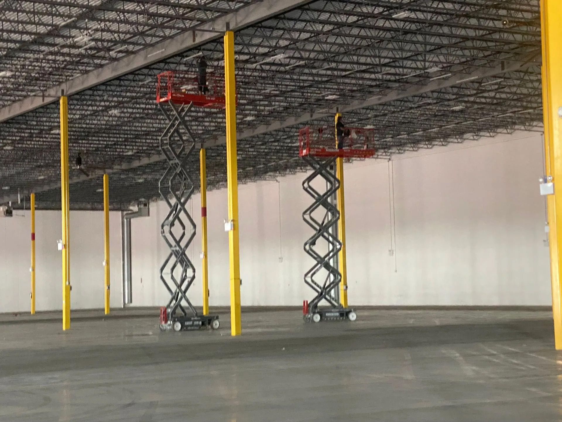 Two scissor lifts are sitting in an empty warehouse.