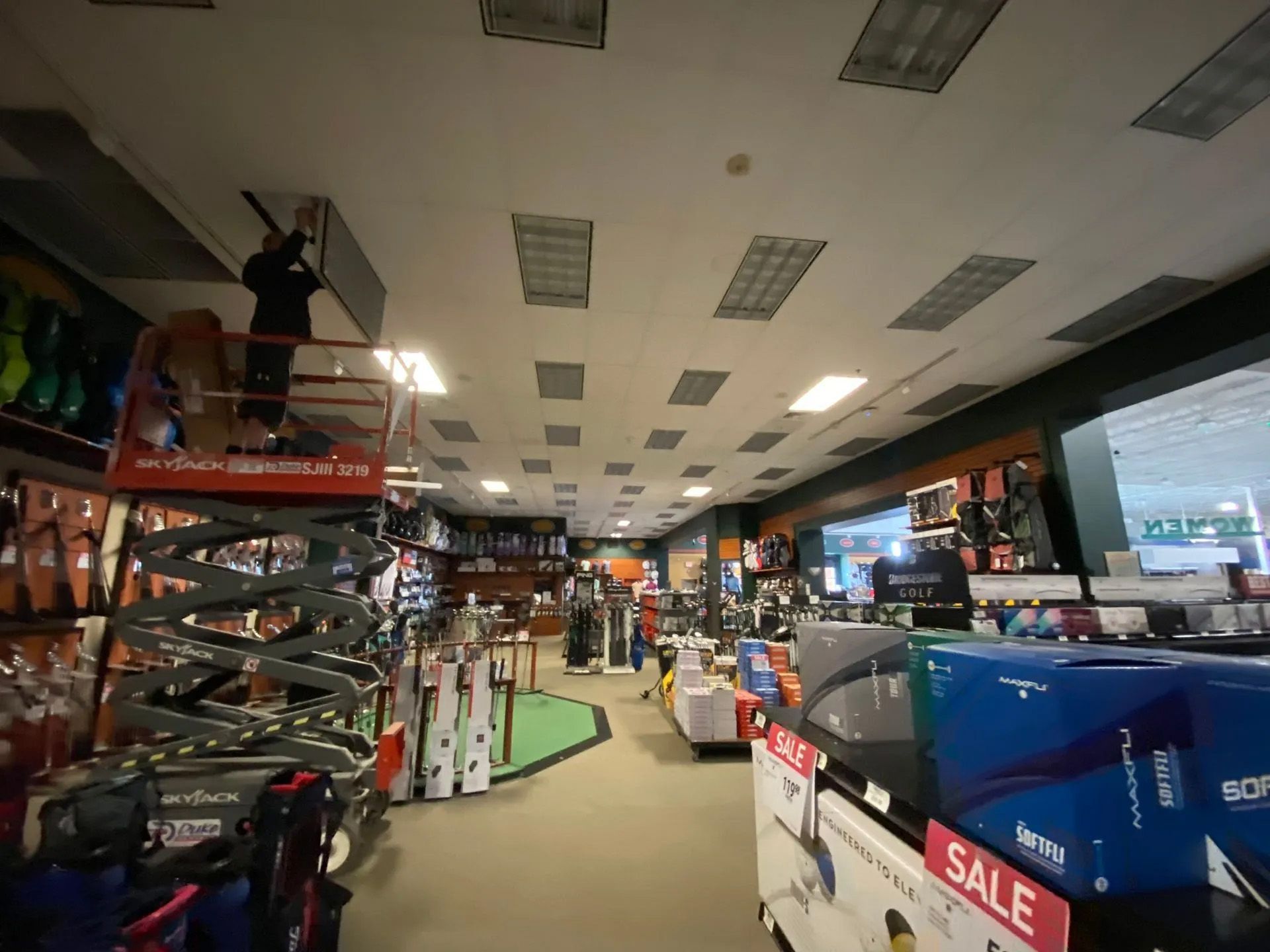 A man is cleaning the ceiling of a store with a sign that says sale