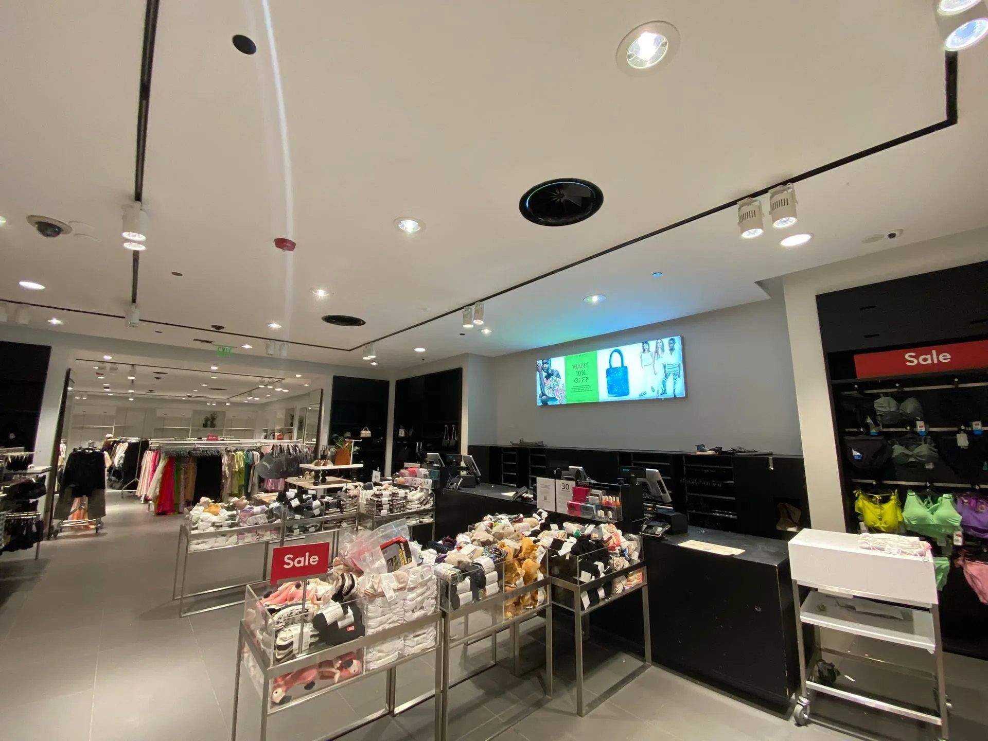 A store filled with lots of clothes and a large screen on the ceiling.
