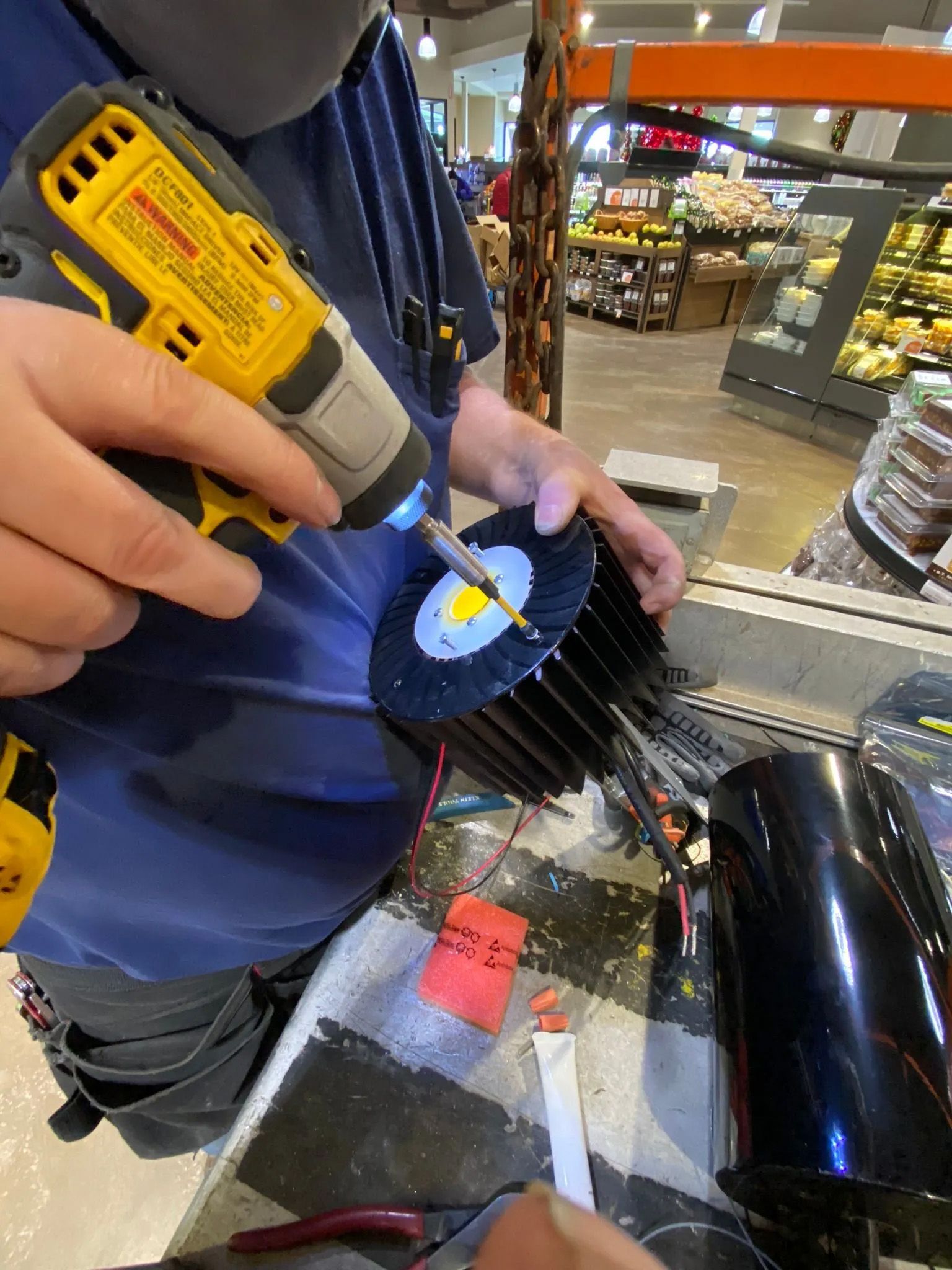 A man is using a drill to fix a lamp in a grocery store.