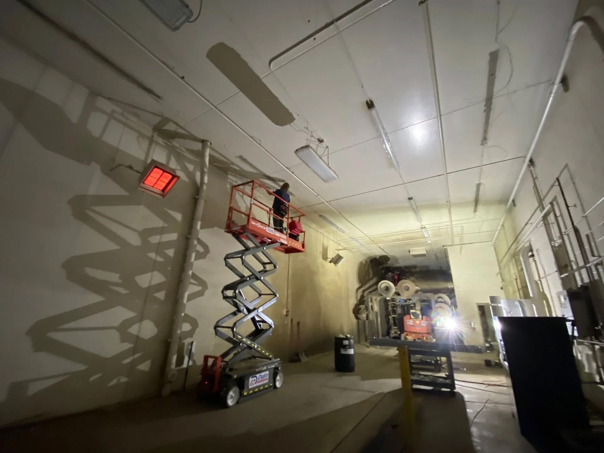 A man is standing on a scissor lift in a dark room.