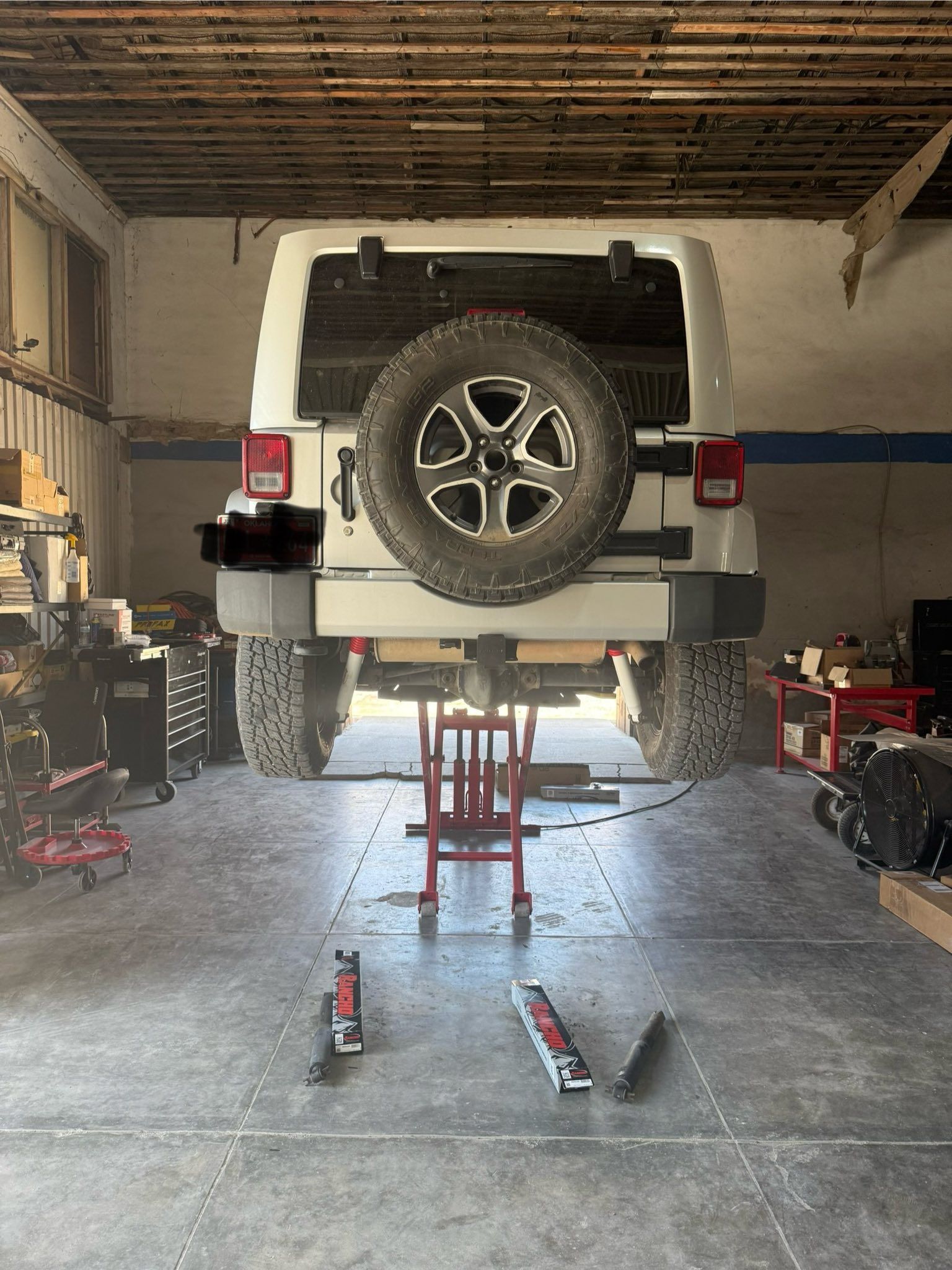 A white jeep is sitting on a lift in a garage.