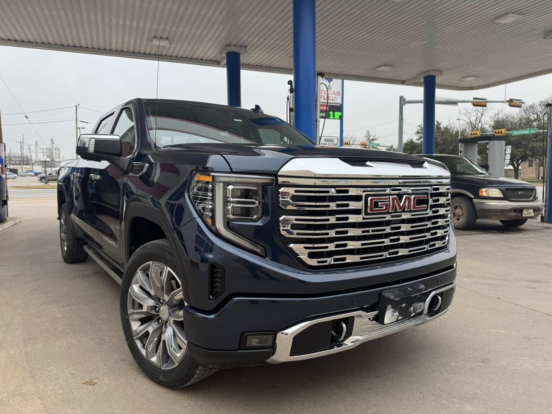 A blue gmc truck is parked in a gas station.