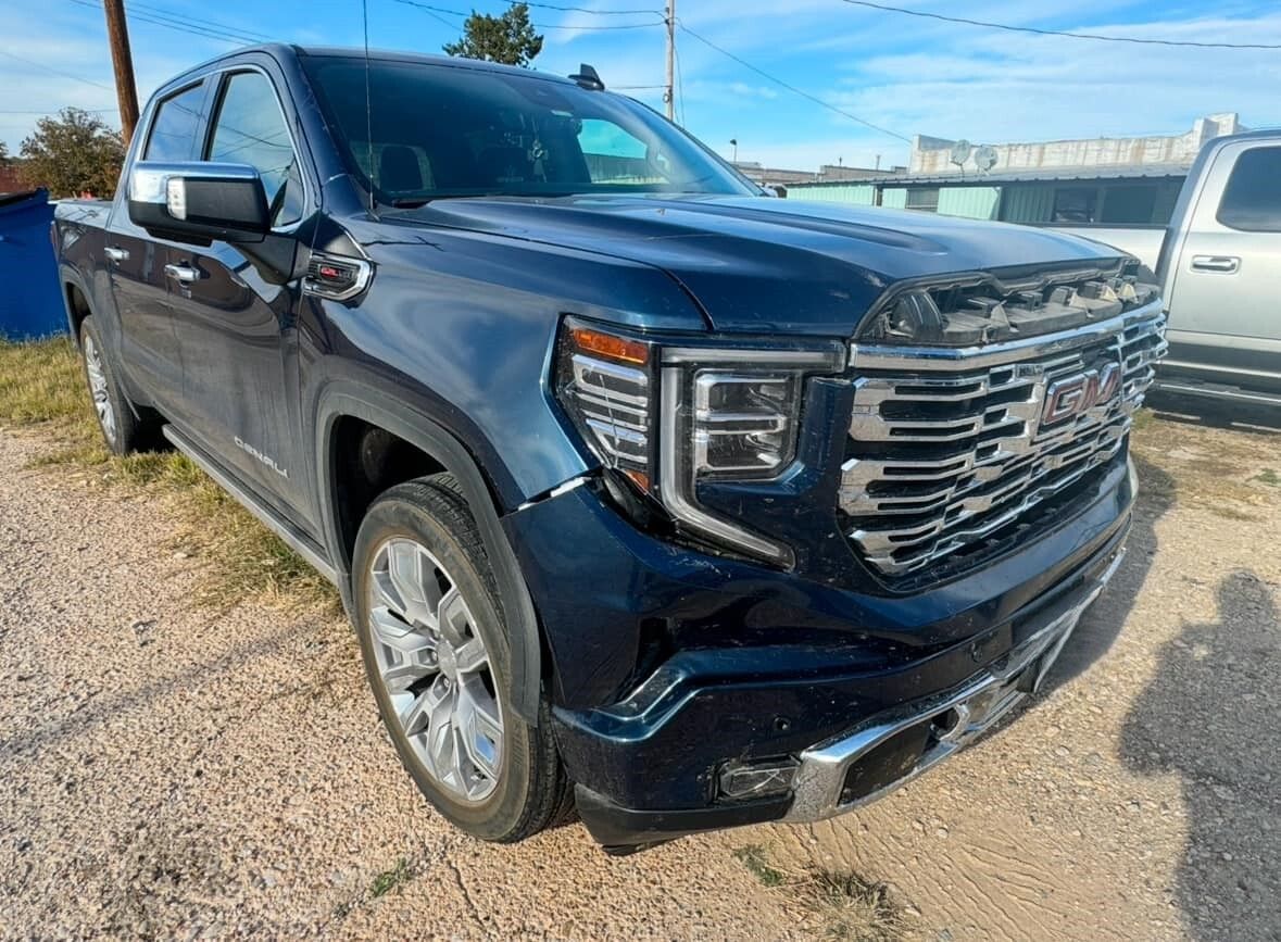 A blue gmc sierra pickup truck is parked in a gravel lot.